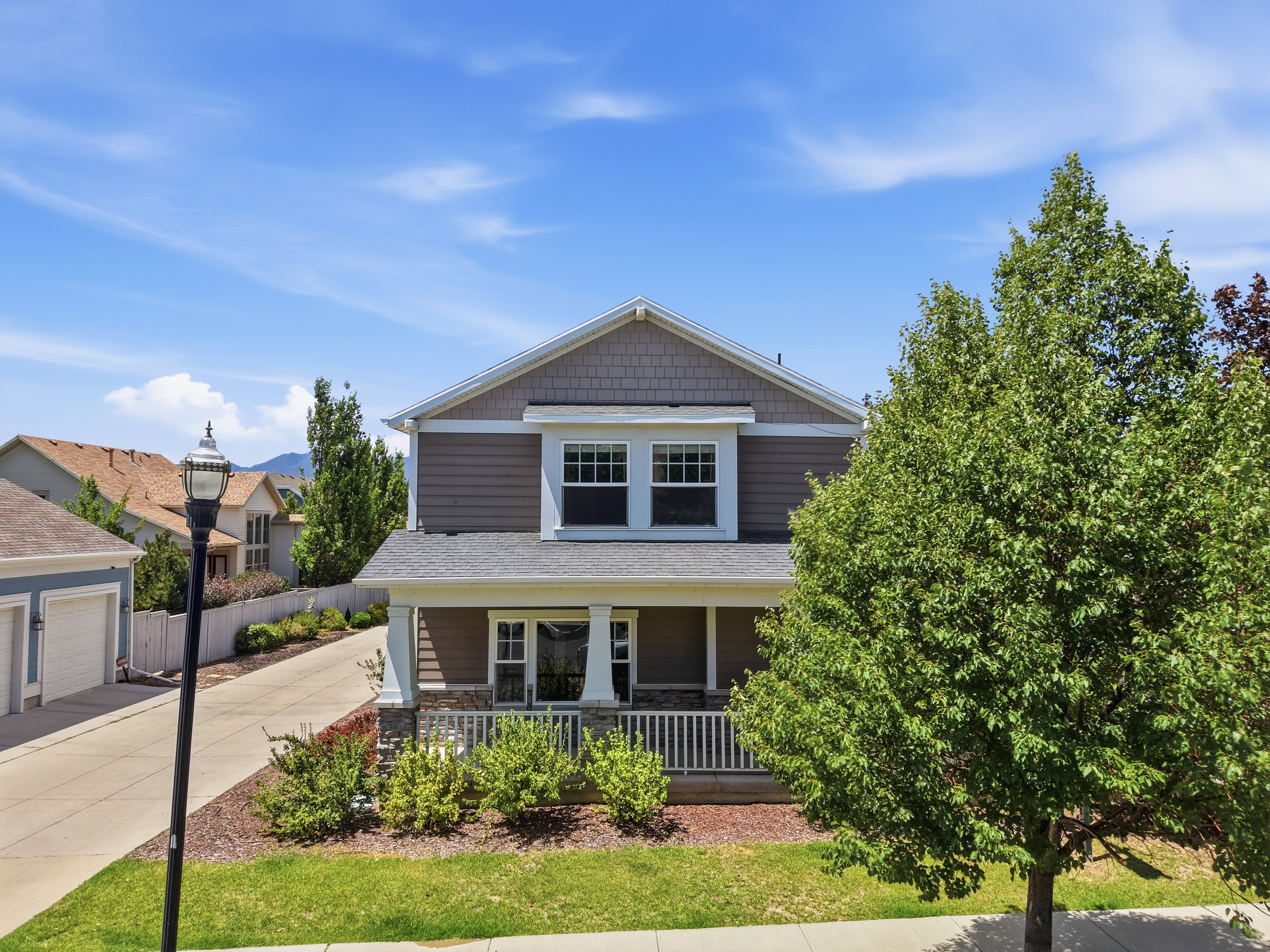 Two-story residence featuring shingle and horizontal siding, a covered front porch with white railing, a gabled roofline, and front landscaping