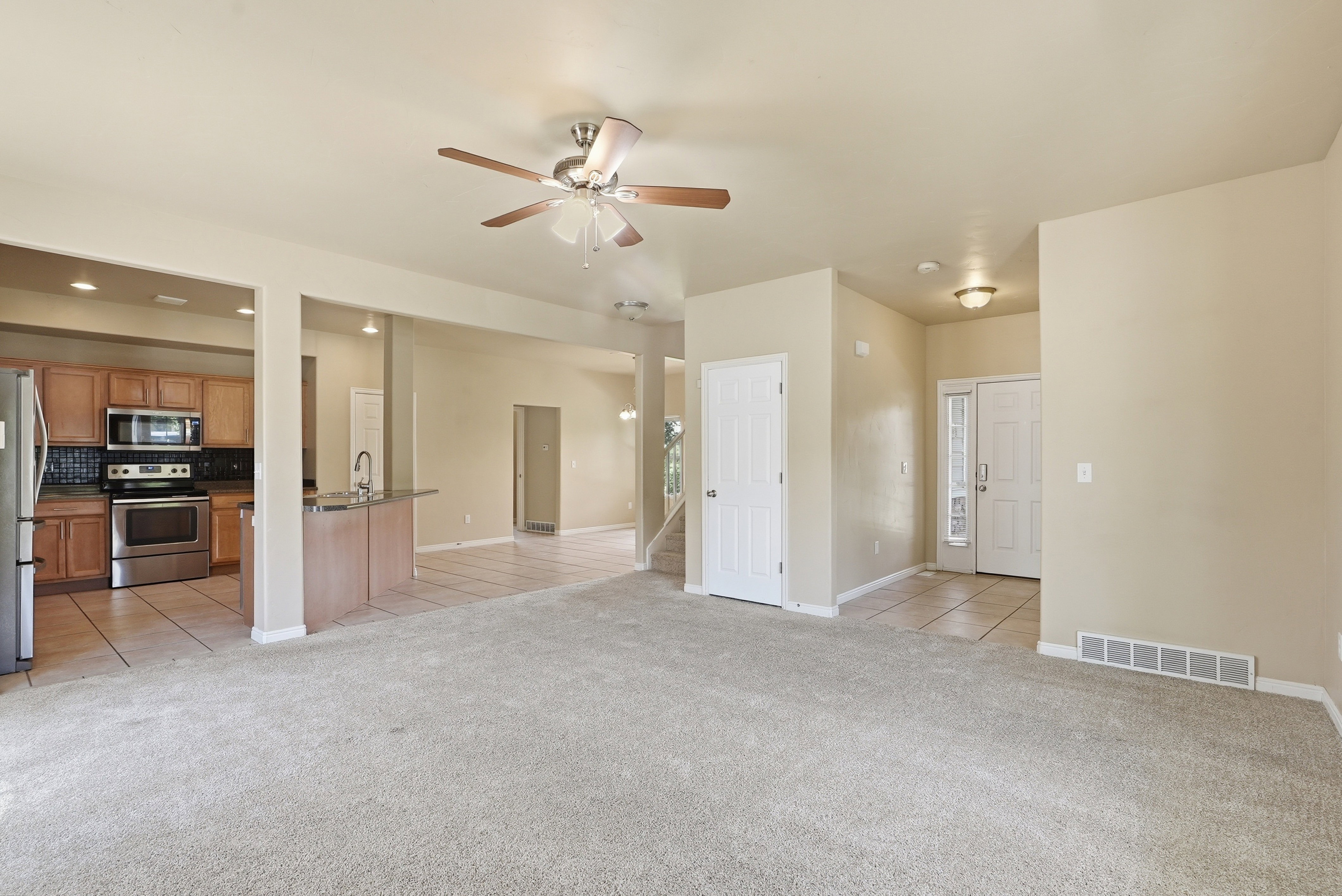 Expansive main living area featuring neutral carpeting, a ceiling fan with light fixture, and recessed lighting