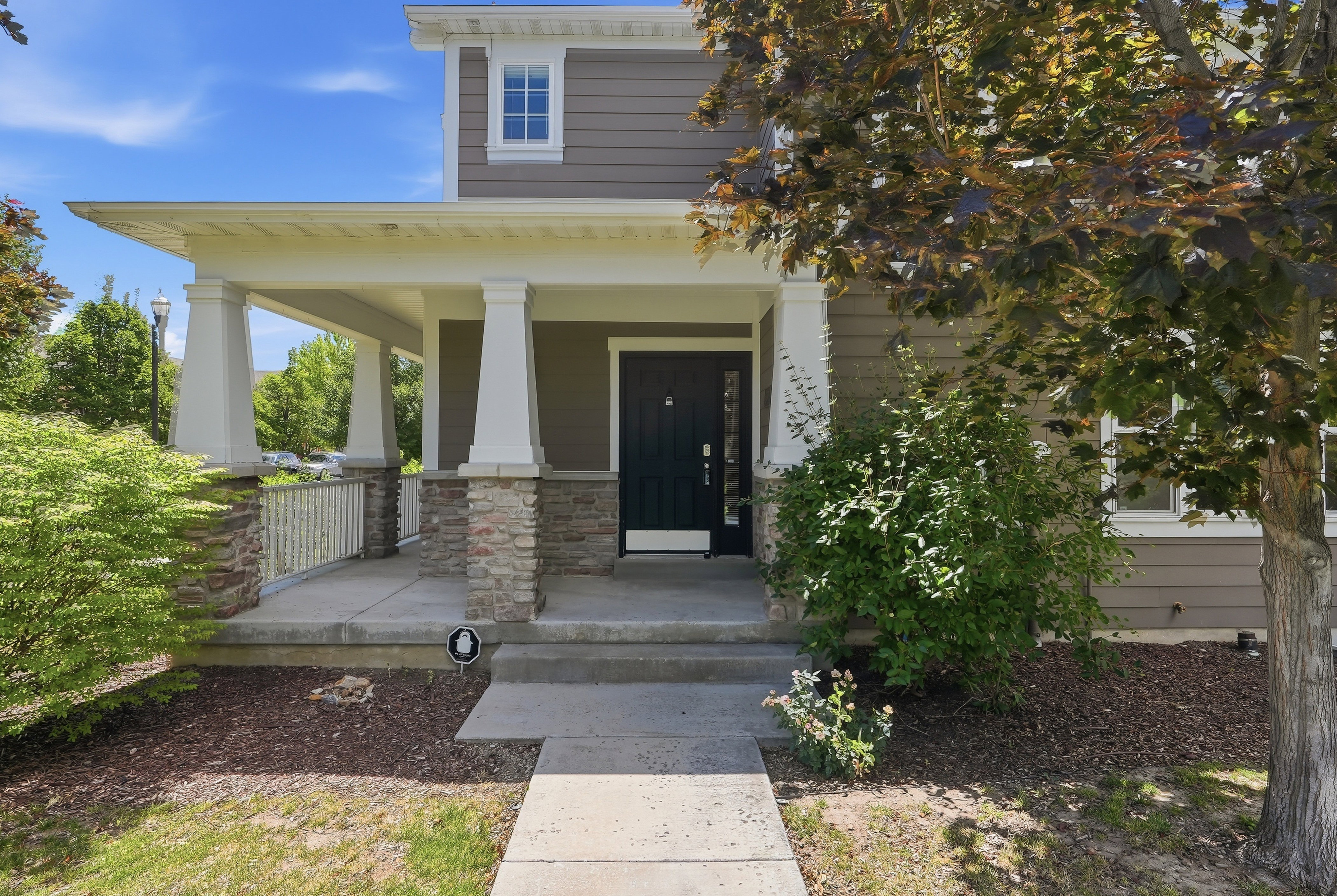 Front exterior featuring a covered porch with stone-clad columns, dark panel siding, and a prominent dark entry door with frosted glass accents
