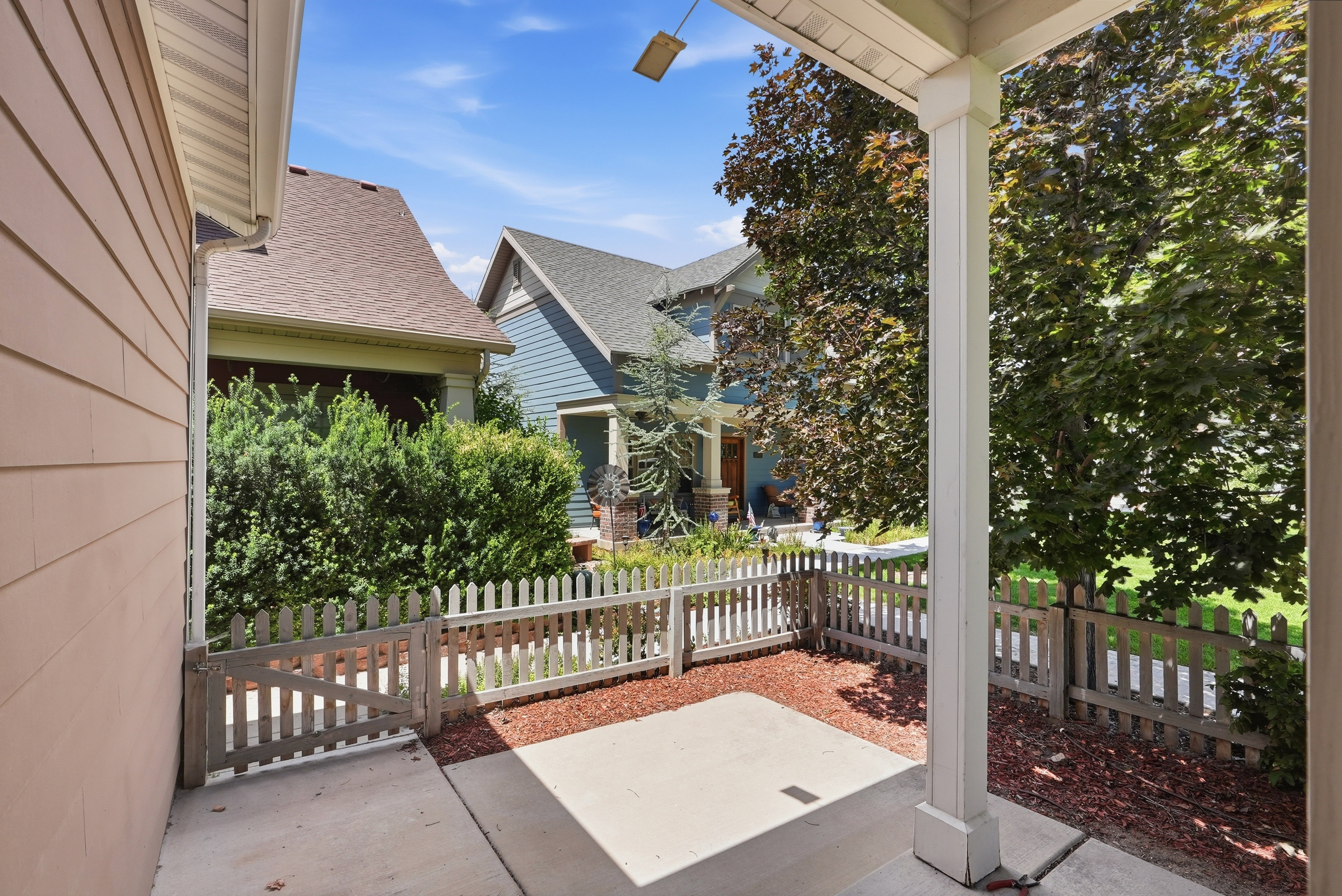 Covered patio with concrete flooring, accented by a white picket fence, a small gate, and decorative red mulch