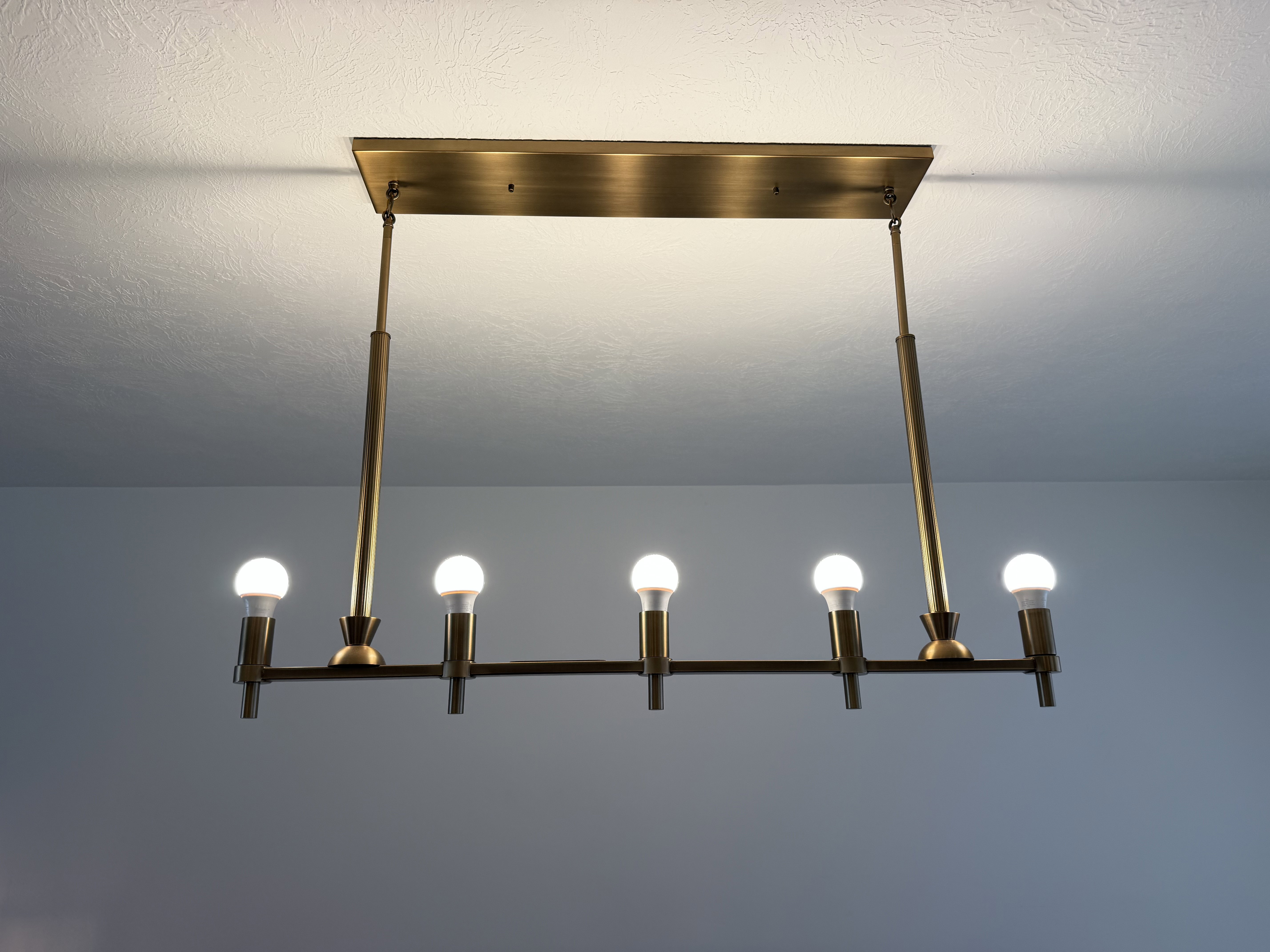Linear chandelier with six exposed bulbs, featuring a brass finish and a rectangular ceiling mount