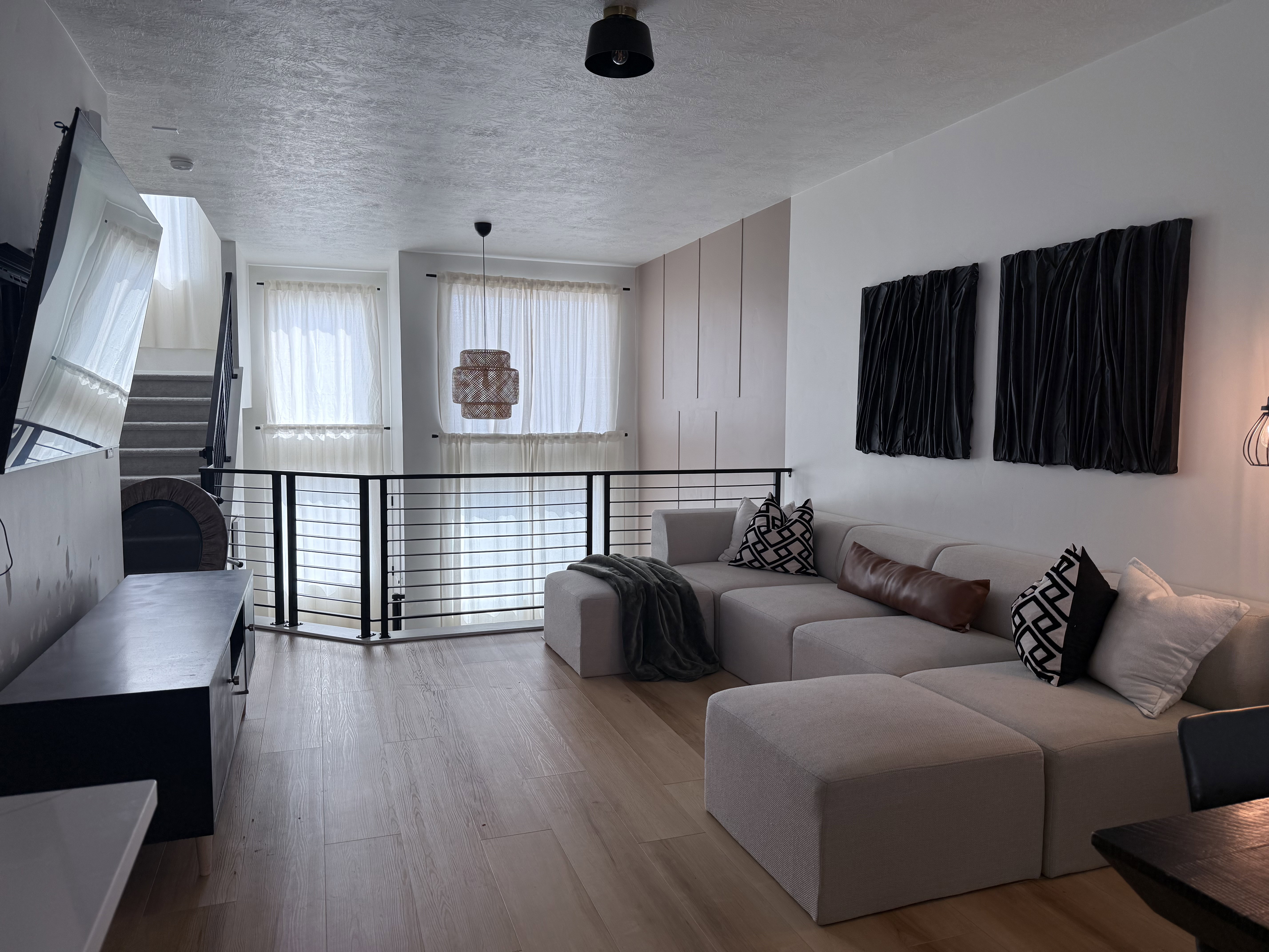 Open-concept living space featuring light wood-finish flooring, a contemporary black metal railing, and white wall paneling