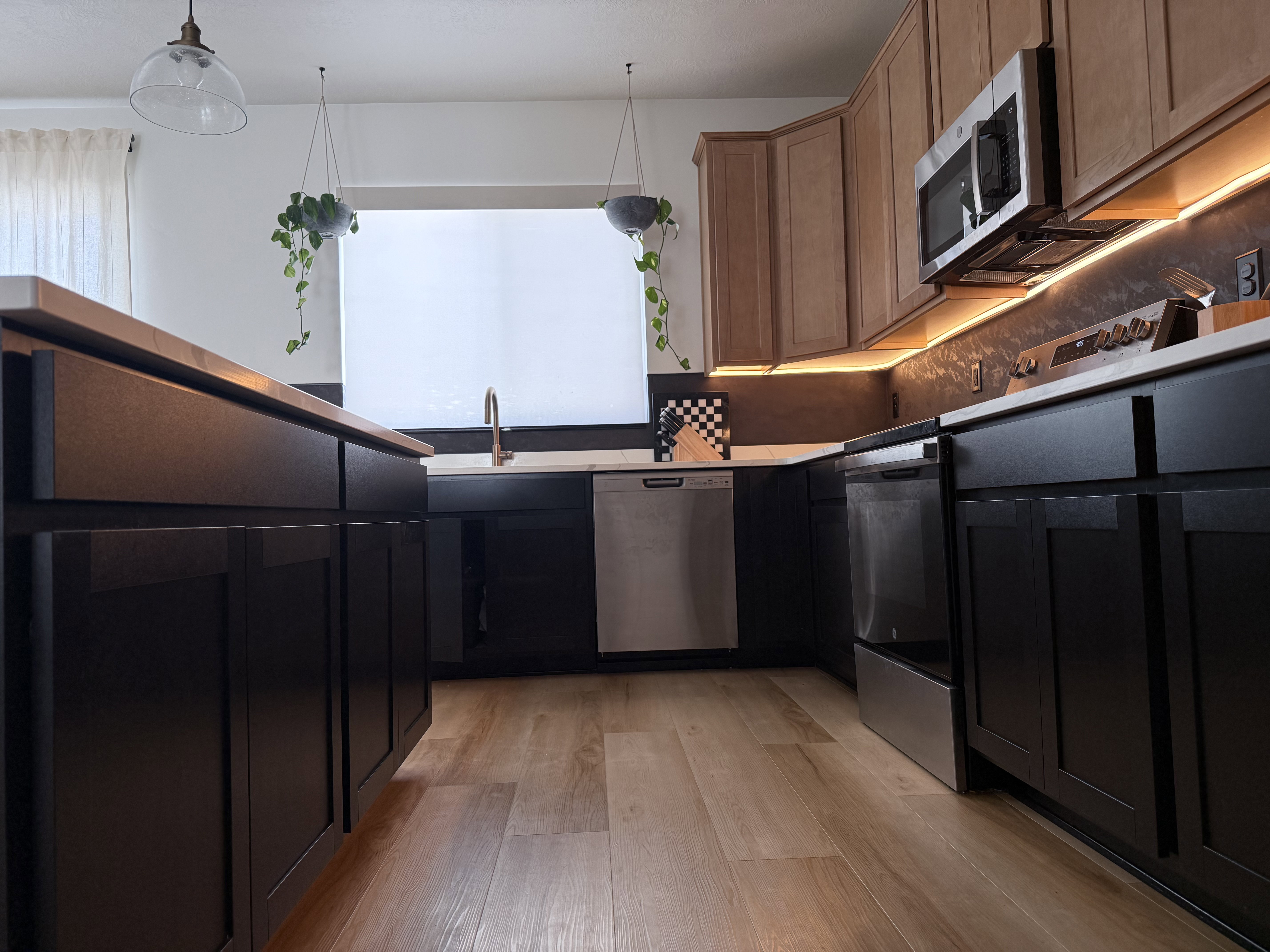 Kitchen featuring wood-finish flooring, two-tone cabinetry with dark lower cabinets and light upper cabinets, stainless steel appliances, a window above the sink, and under-cabinet lighting