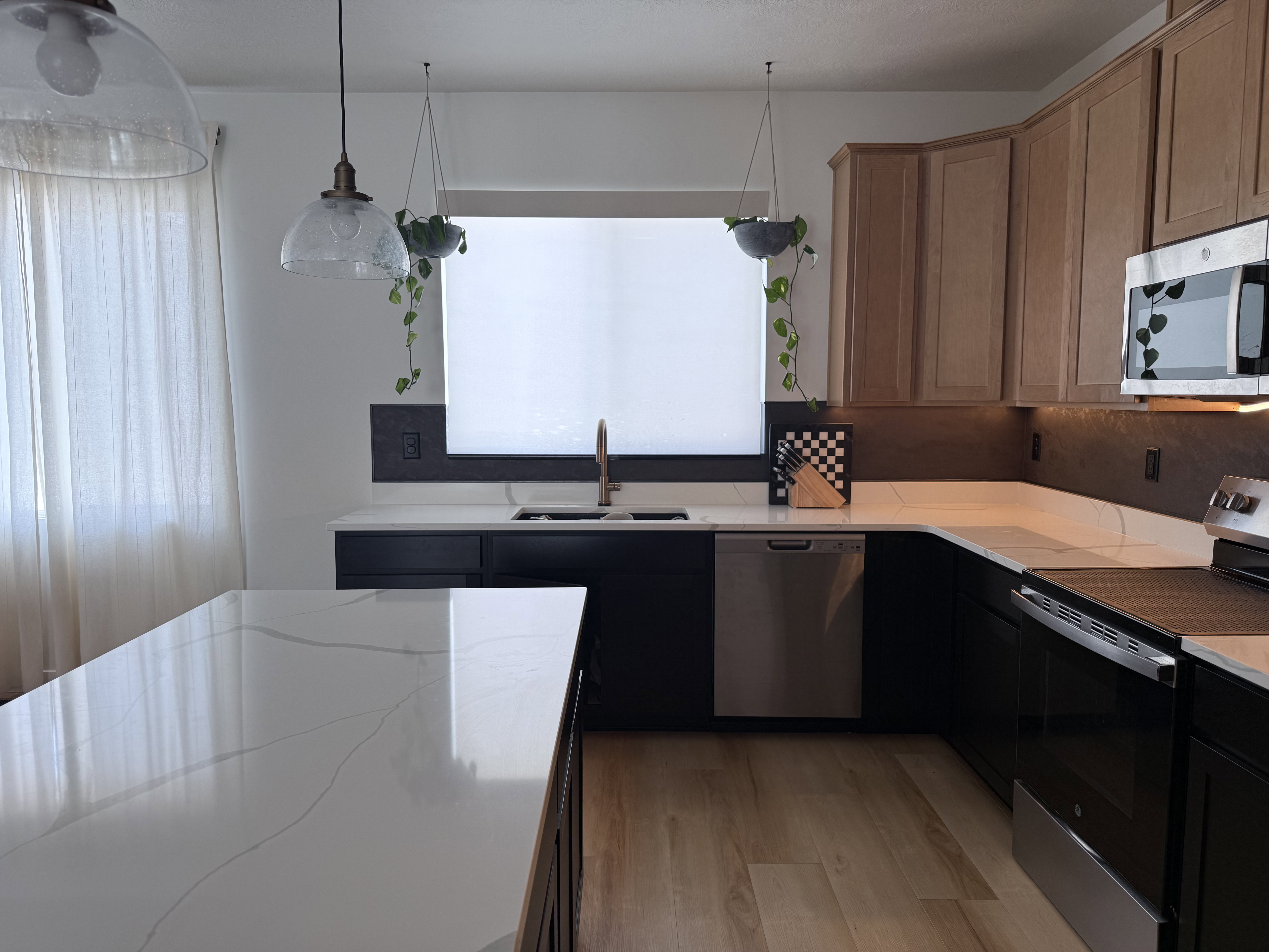Modern kitchen featuring white countertops with subtle veining, dark lower cabinetry, and light wood-finish upper cabinets