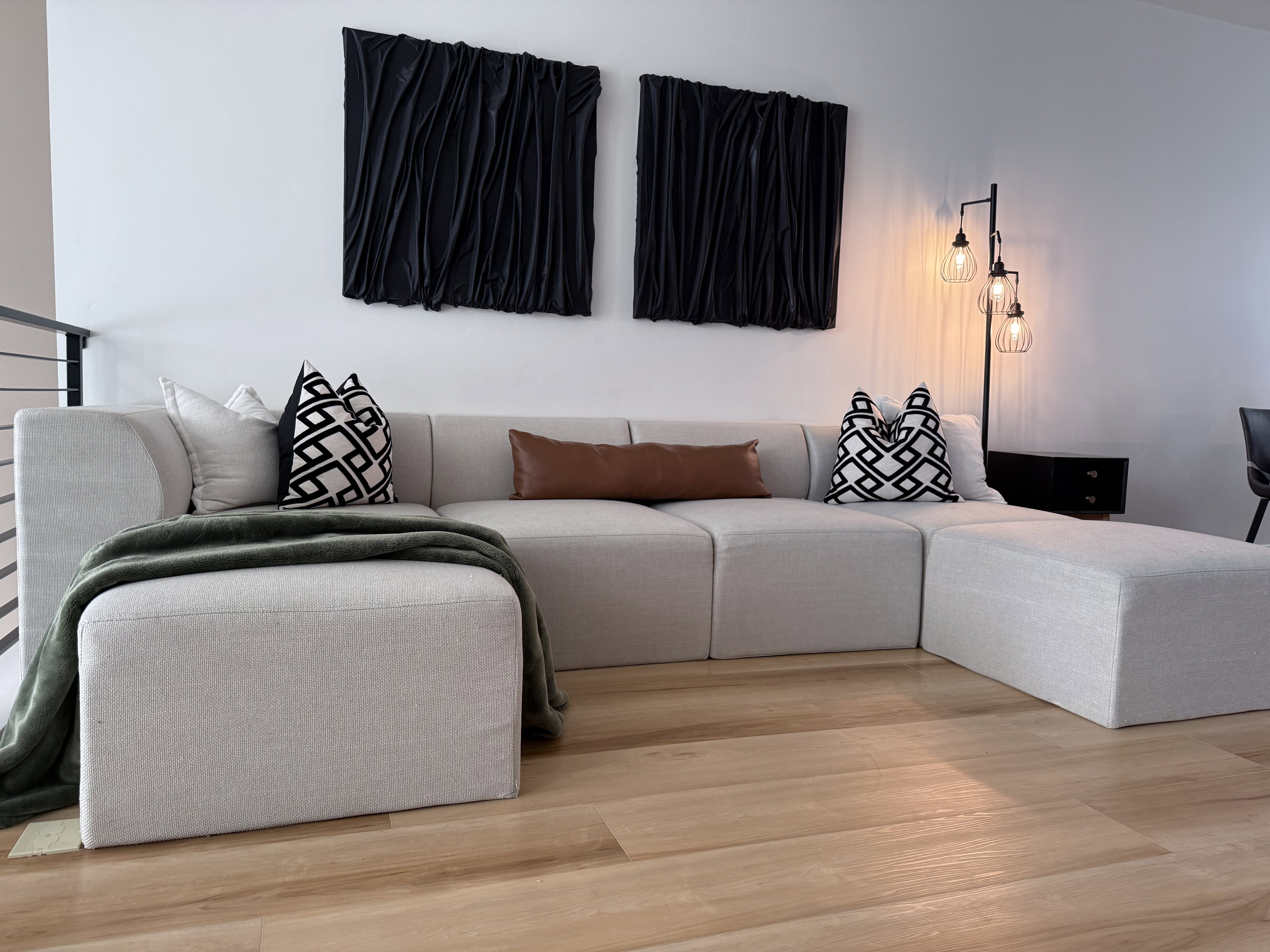 Spacious open-concept area featuring light wood-finish flooring, a contemporary industrial-style floor lamp, and a modern metal railing
