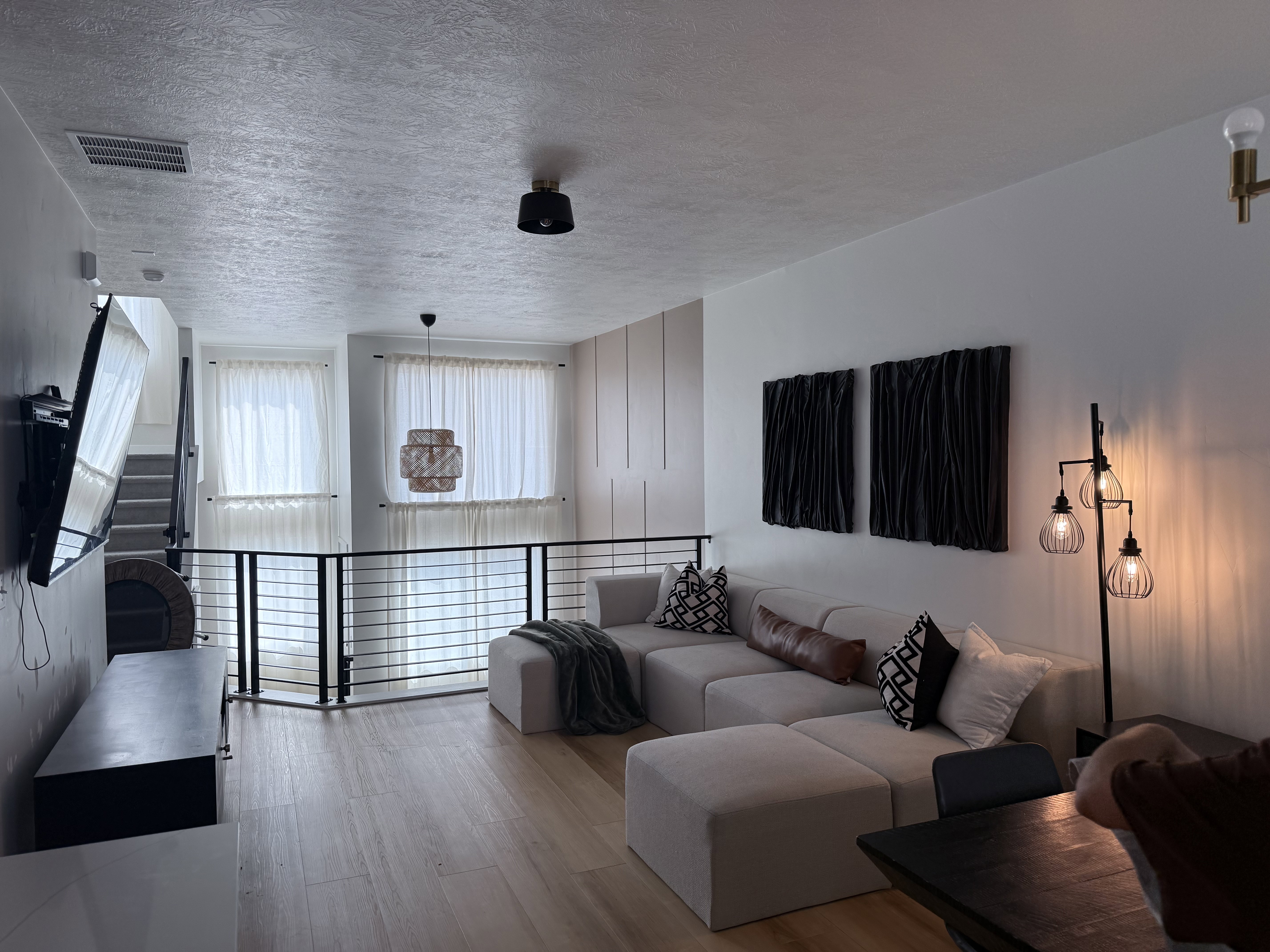 Open-concept living area with wood-finish flooring, a contemporary railing system, and multiple windows with sheer window treatments