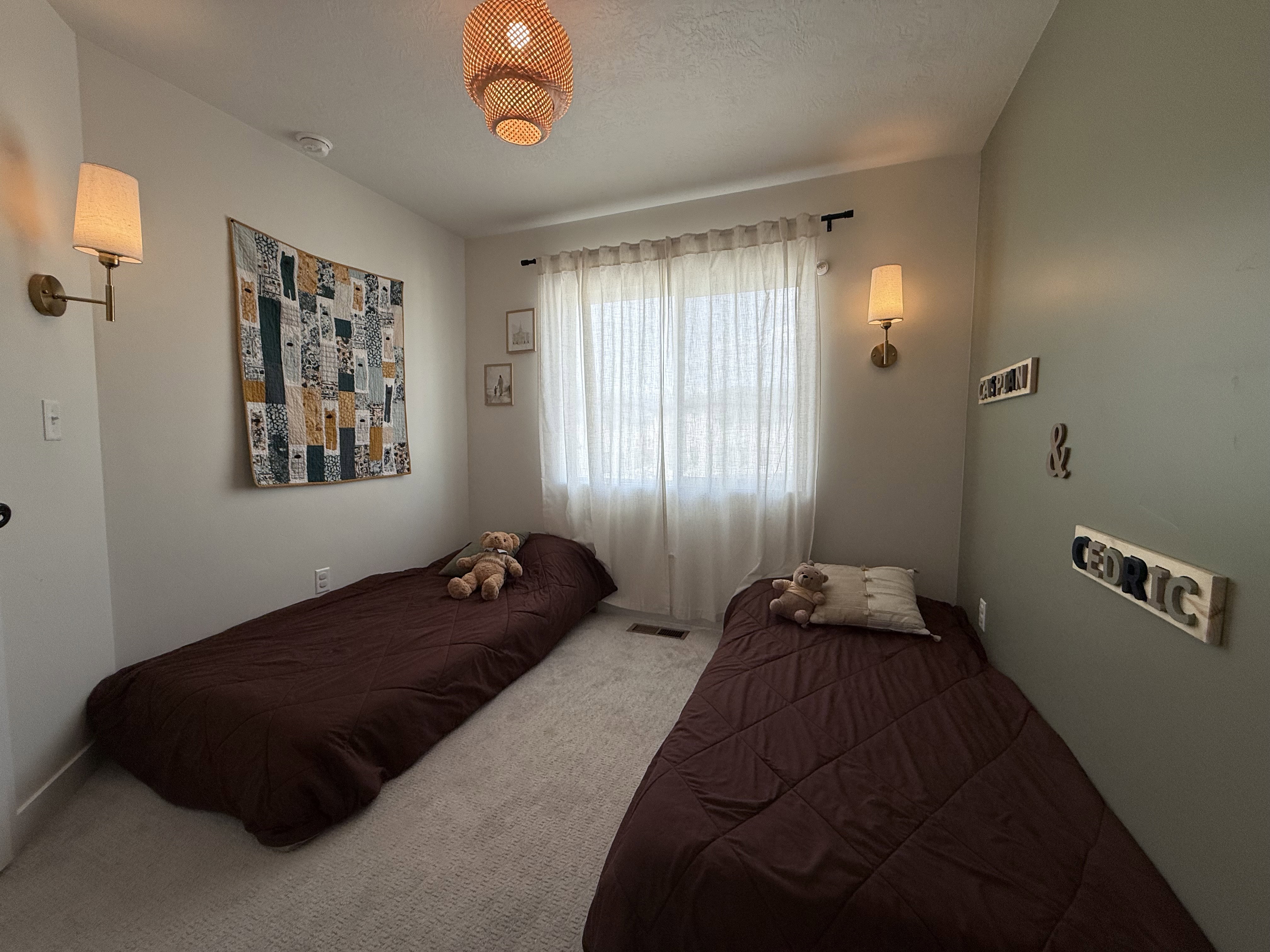 Carpeted room featuring a window with sheer curtains, two wall-mounted sconces, and a woven ceiling light fixture