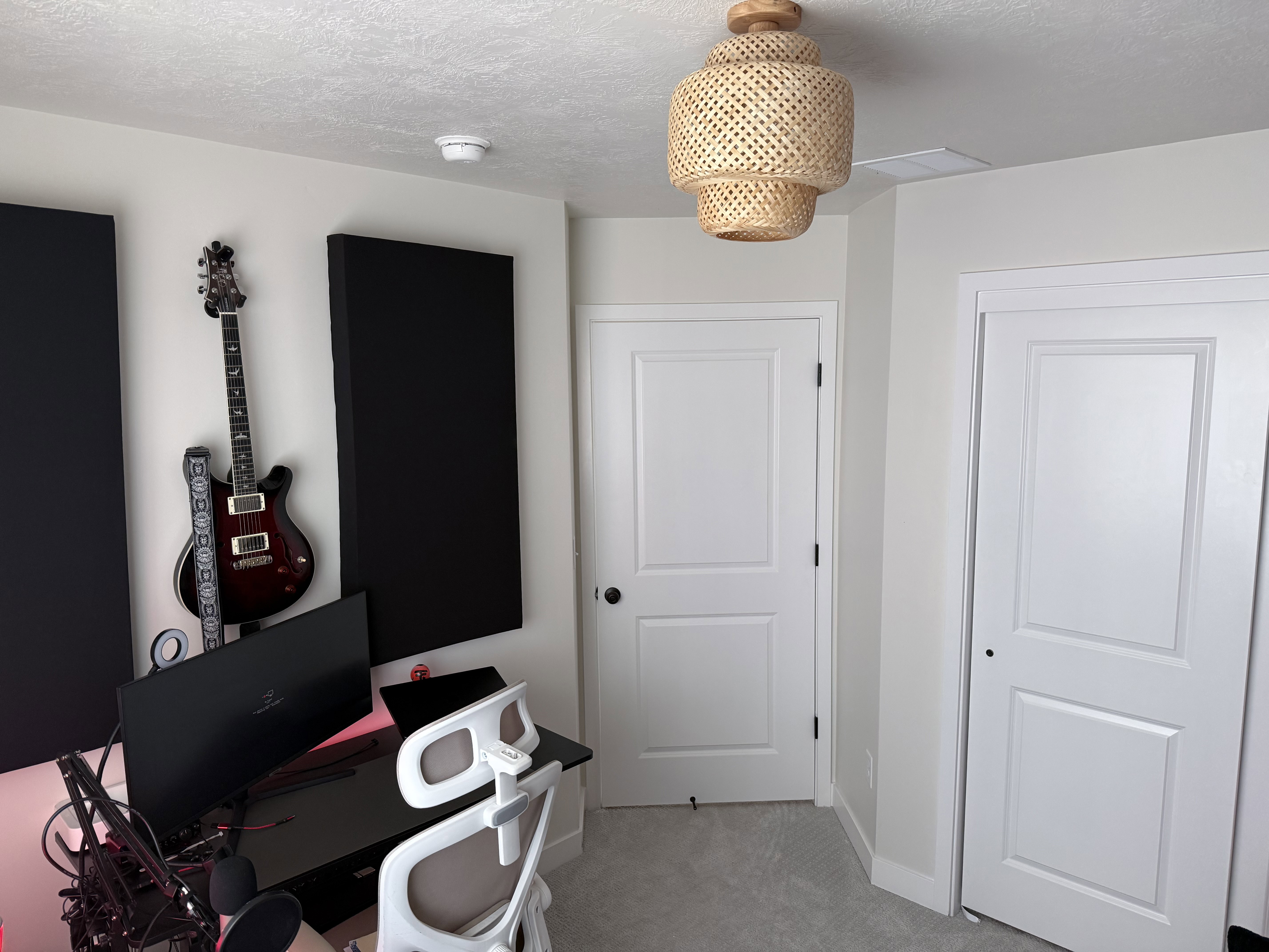 Room featuring two white two-panel doors with black hardware, light neutral carpet, and a textured natural wood semi-flushmount ceiling light fixture