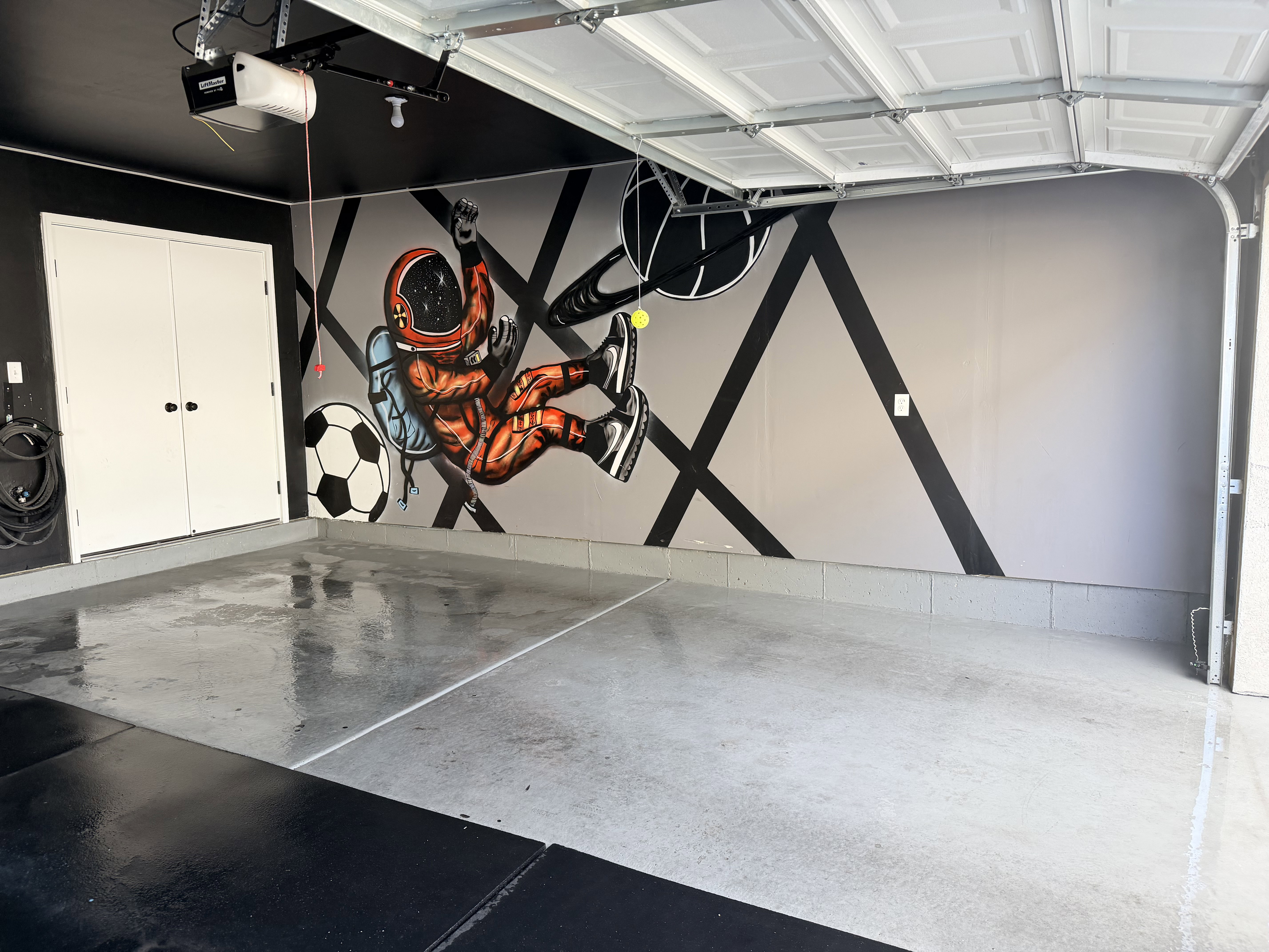 Garage space featuring epoxy flooring, a decorative wall mural, and dual white storage doors