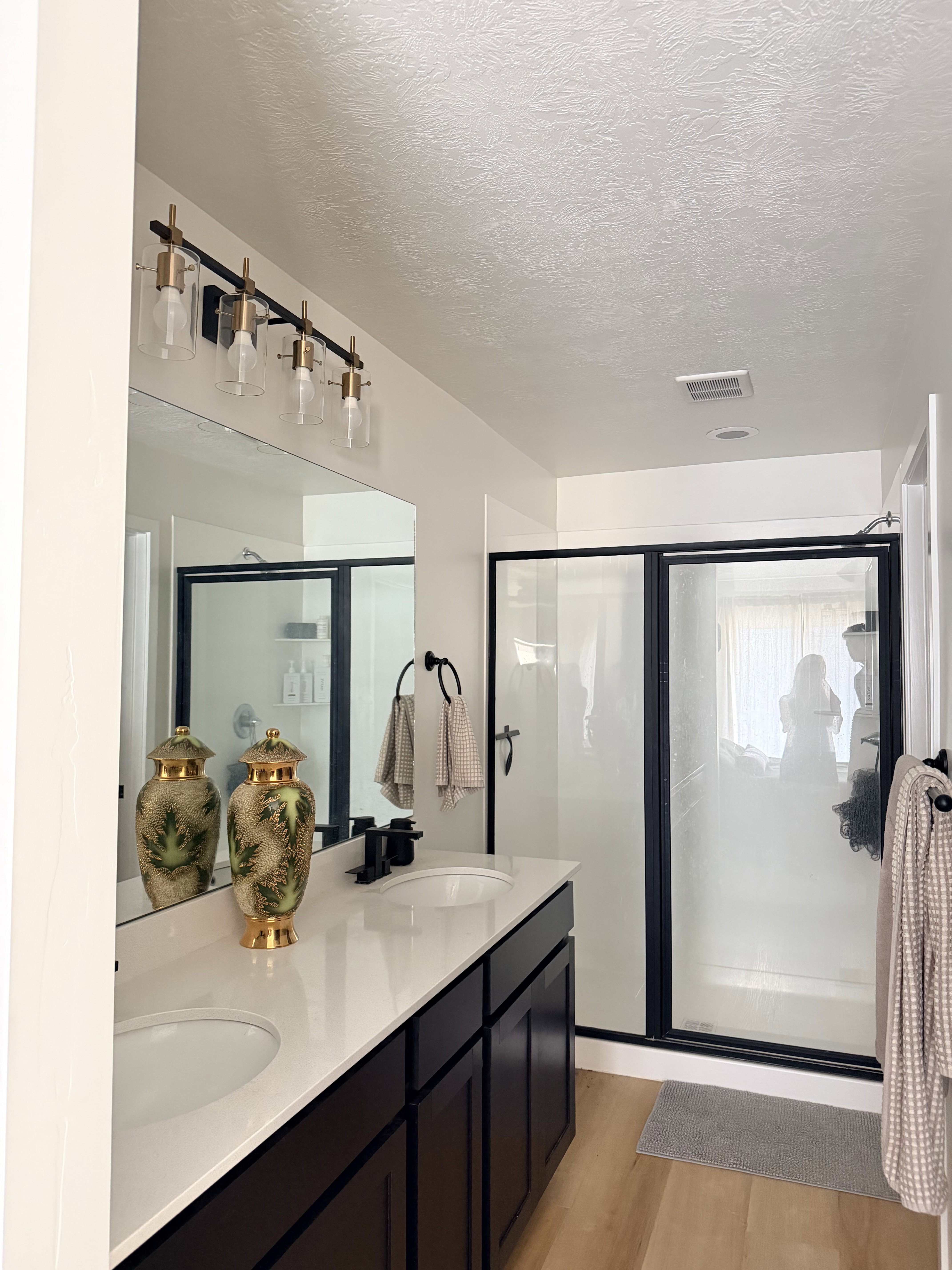Bathroom featuring a dual vanity with dark wood cabinetry and white countertops, matte black faucets, and a large frameless mirror