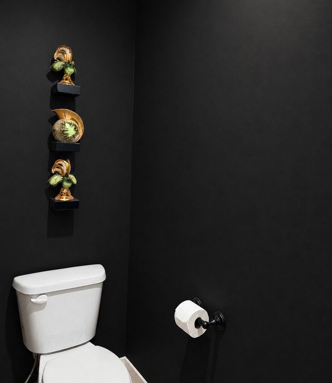 White porcelain toilet with a dark-finished toilet paper holder against a black wall