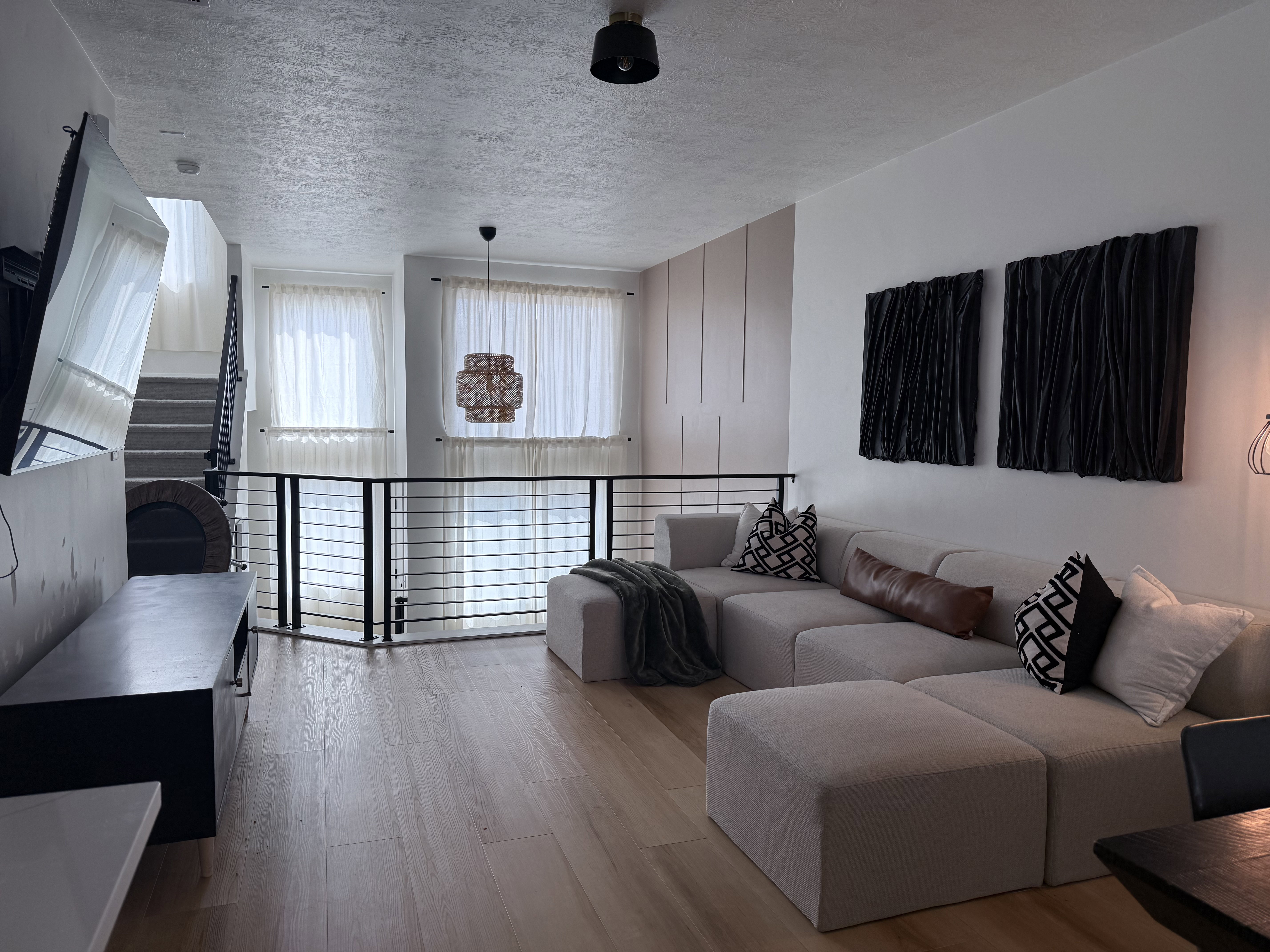 Open-concept living space featuring wood-finish flooring, a contemporary black metal railing, and high ceilings