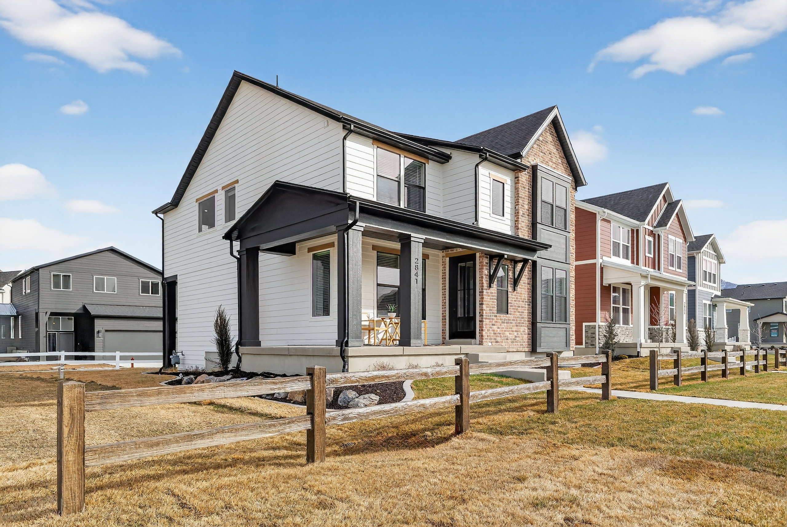 Two-story residence featuring a covered front porch with dark trim, white siding, and brick accents