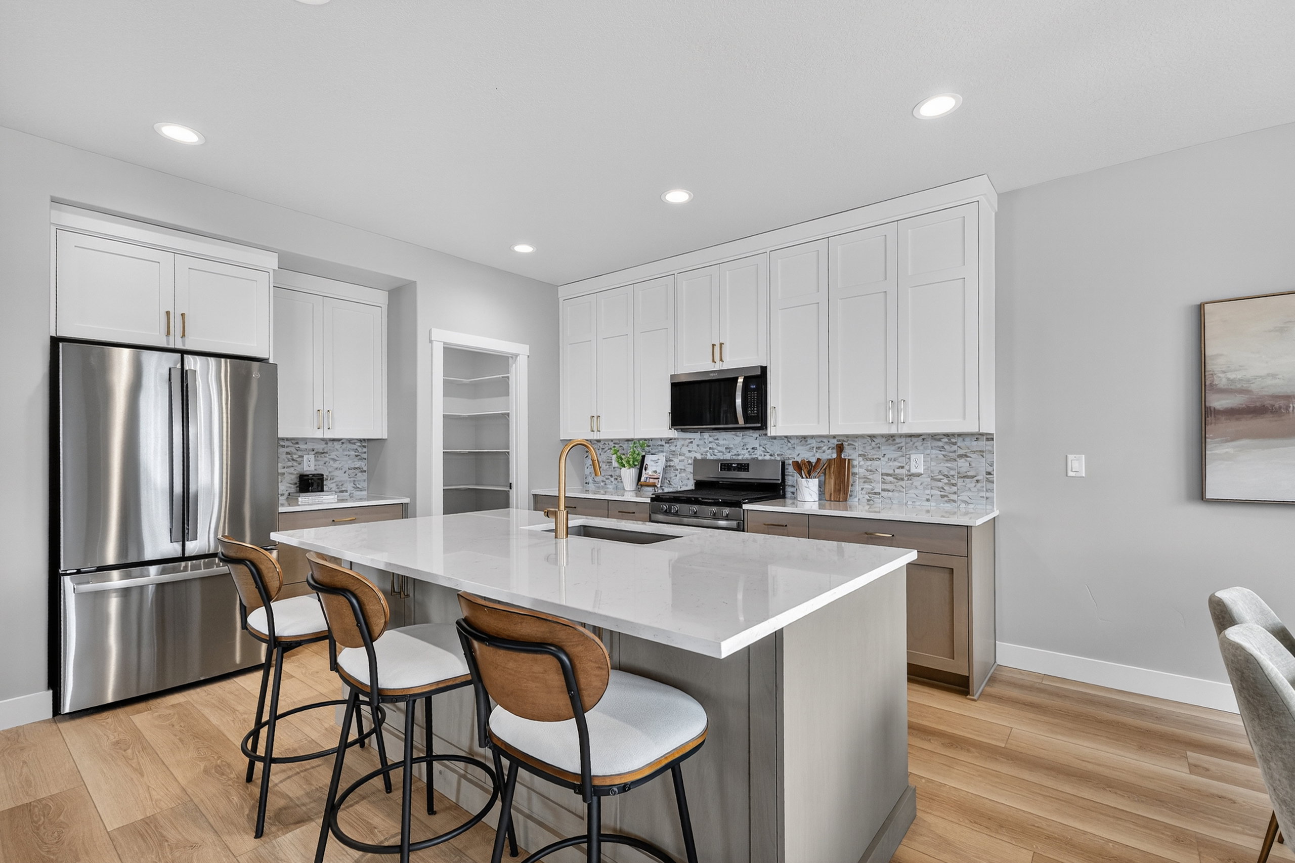 Kitchen featuring a central island with countertop seating, stainless steel appliances, two-tone cabinetry, a tile backsplash, and wood-finish flooring