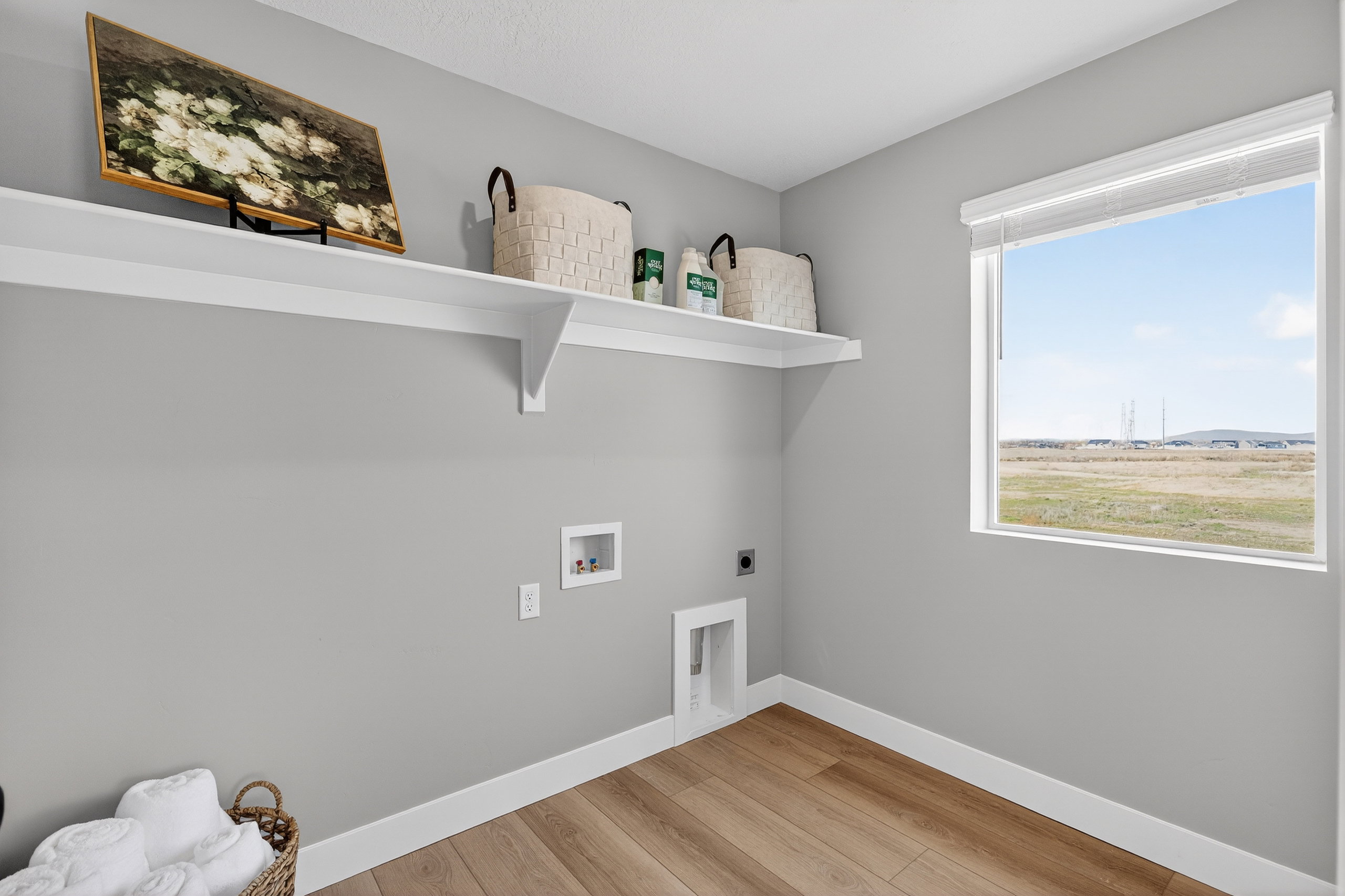 Laundry area featuring light gray walls, wood-finish flooring, and white baseboards