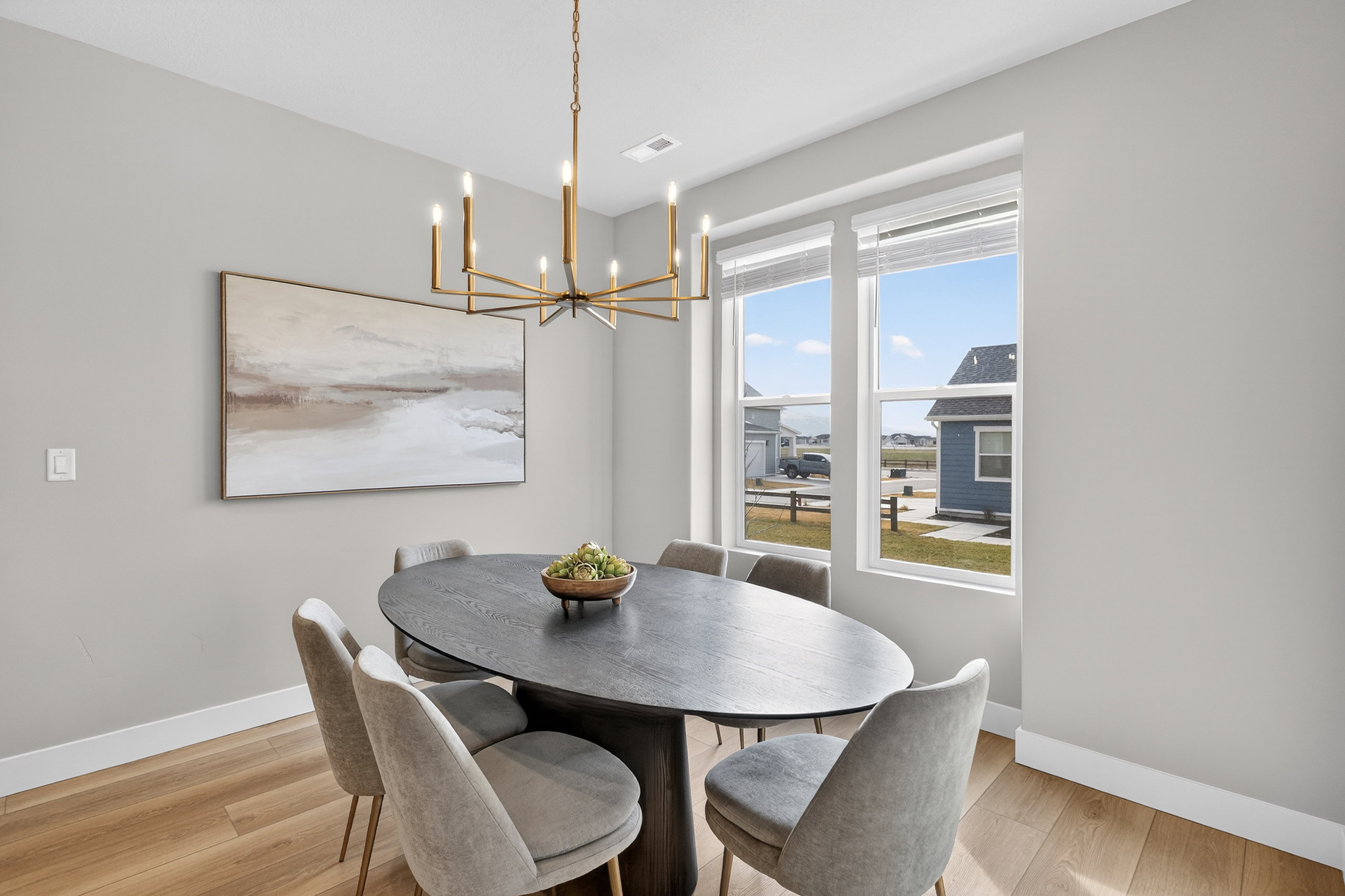 Spacious dining area featuring light wood-finish flooring, a contemporary brass chandelier, a large picture window, and neutral wall tones