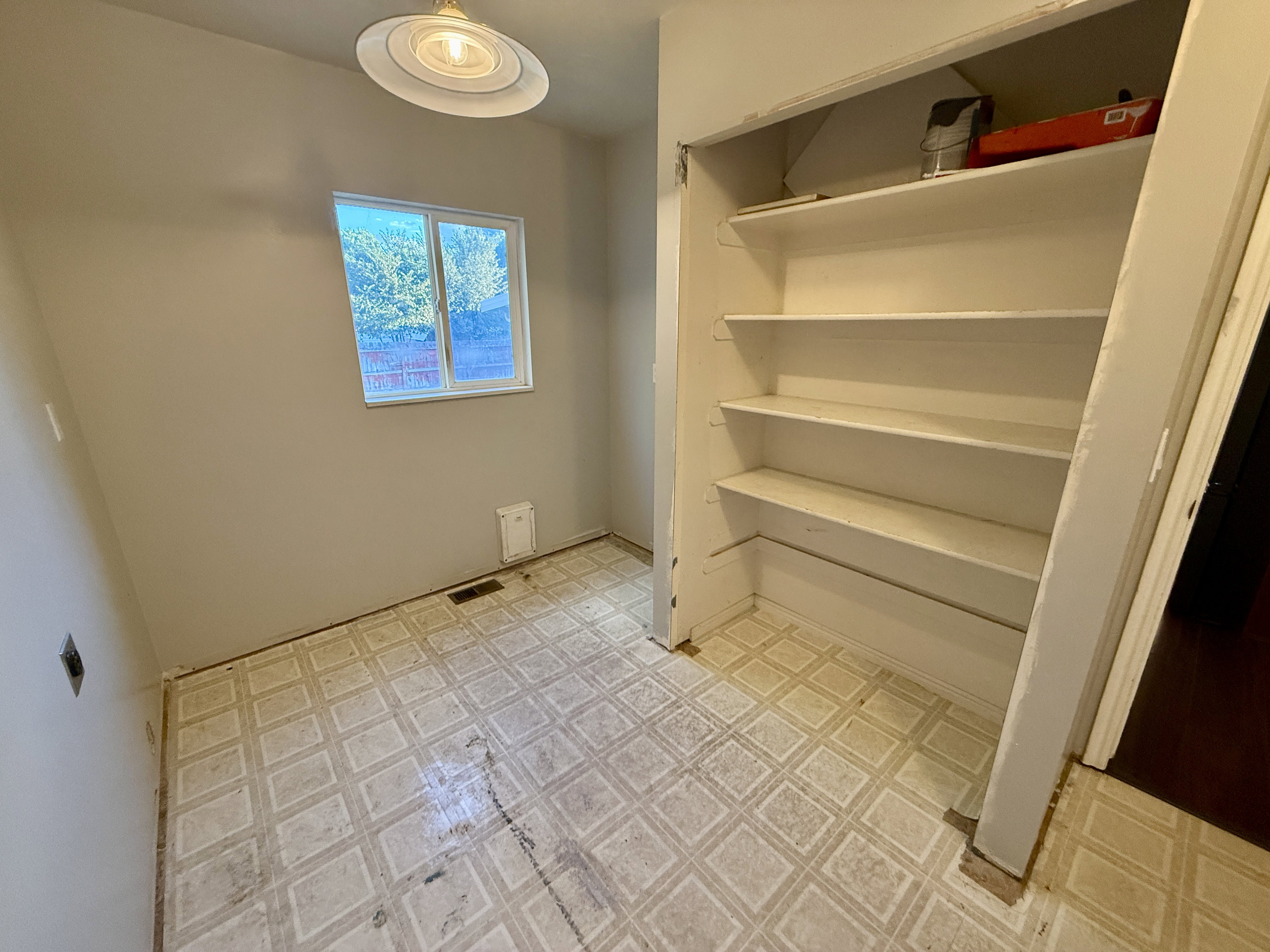 Utility room featuring a window, built-in shelving, patterned flooring, a wall vent, and an overhead light fixture