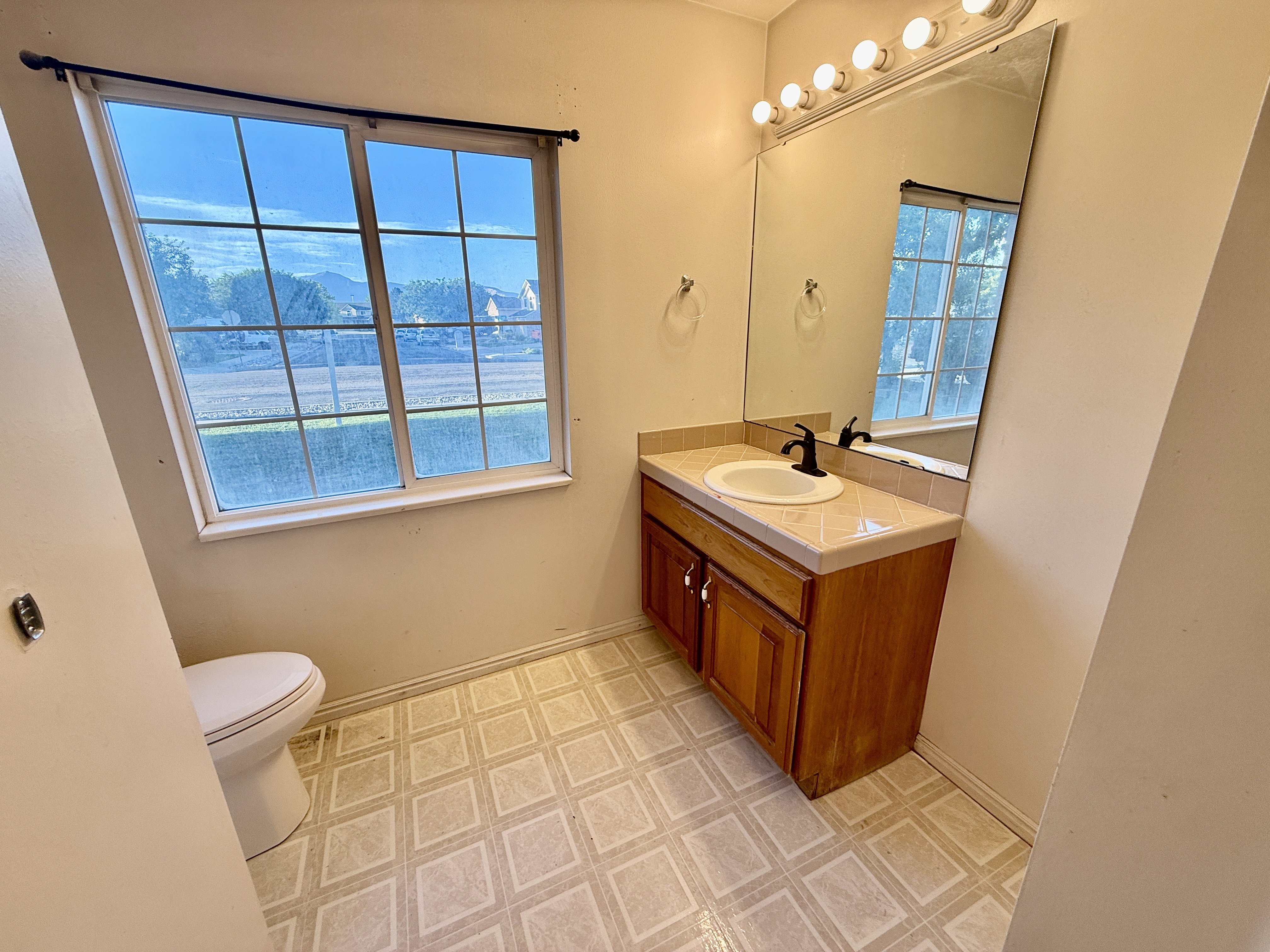 Bathroom featuring a window with grid pattern, a single vanity with wood-finish cabinetry, and a large wall-mounted mirror with overhead lighting