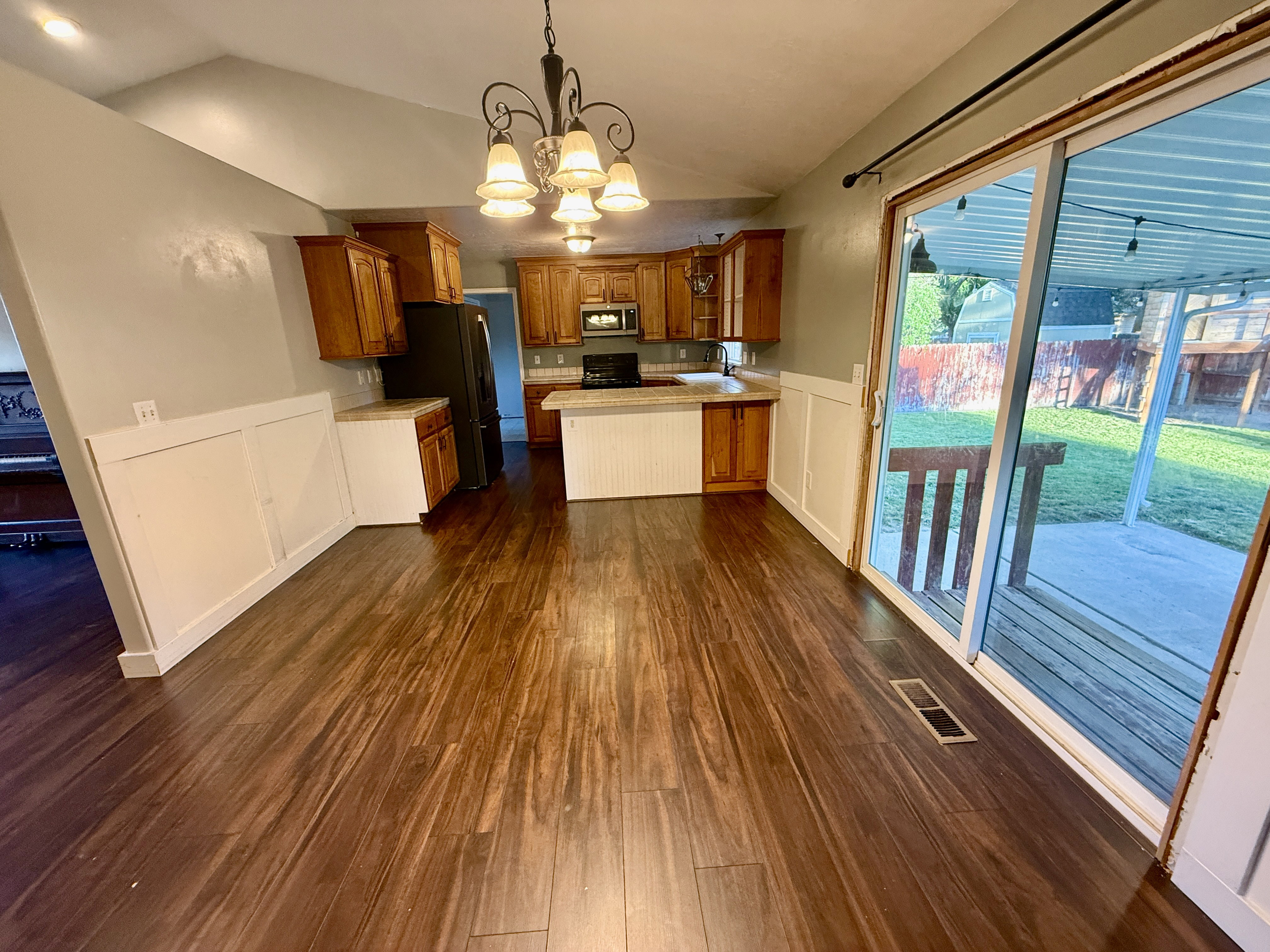 Spacious dining area featuring wood-finish flooring, a decorative chandelier, and white wainscoting