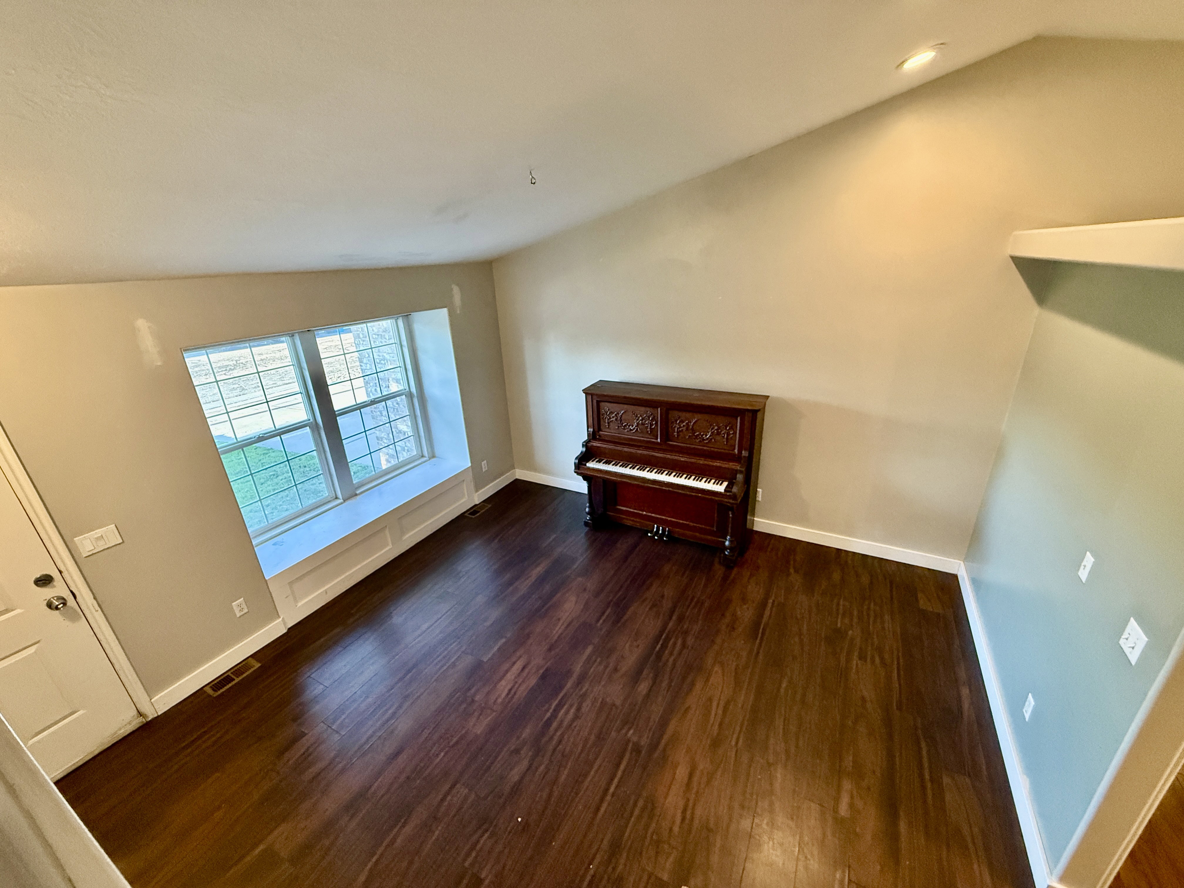 Spacious living area featuring rich wood-finish flooring, a vaulted ceiling with recessed lighting, and a prominent window seat