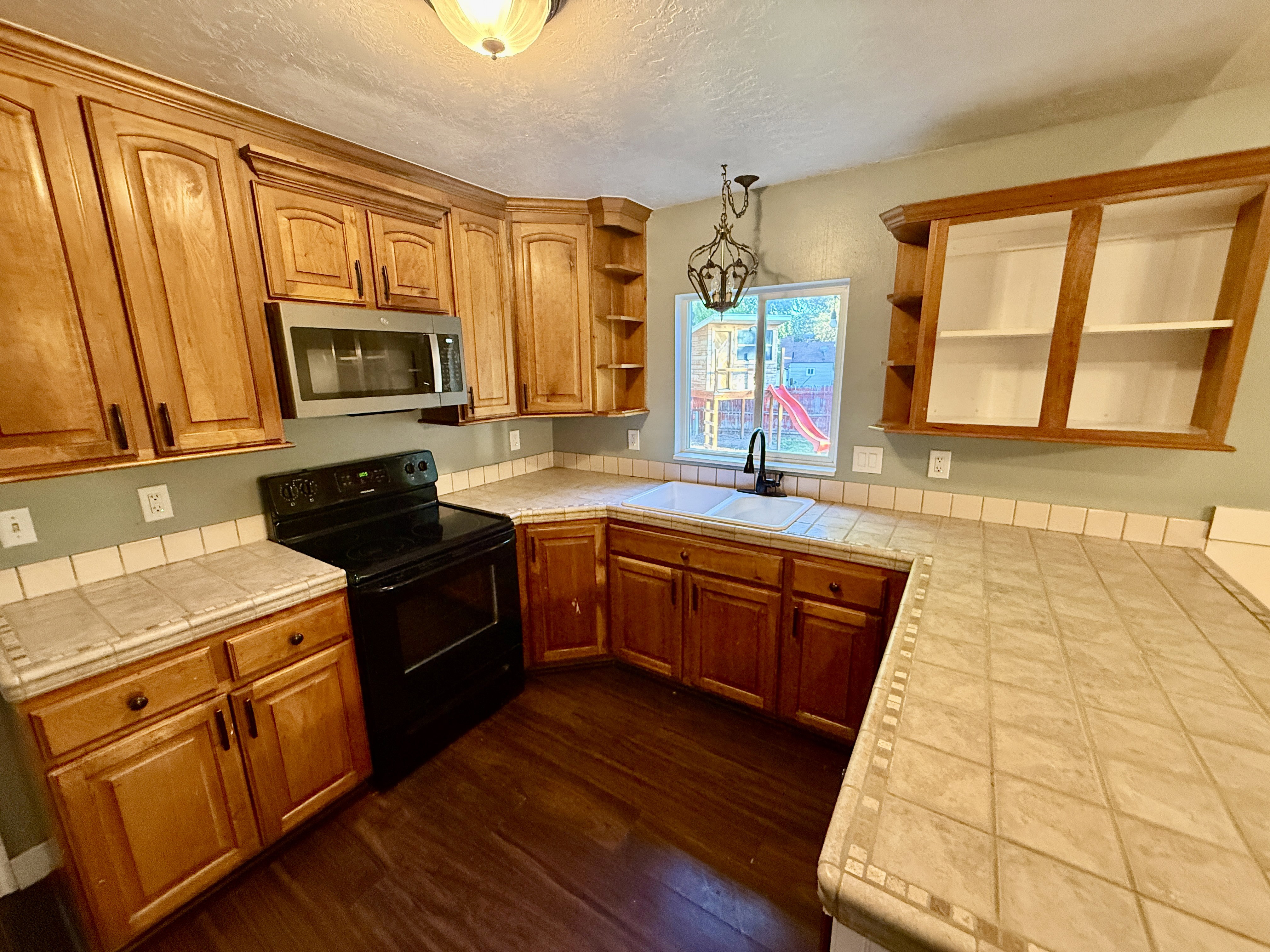 Kitchen featuring wood-finish cabinetry, tile countertops, a double basin sink with a gooseneck faucet, a built-in microwave, and wood-finish flooring