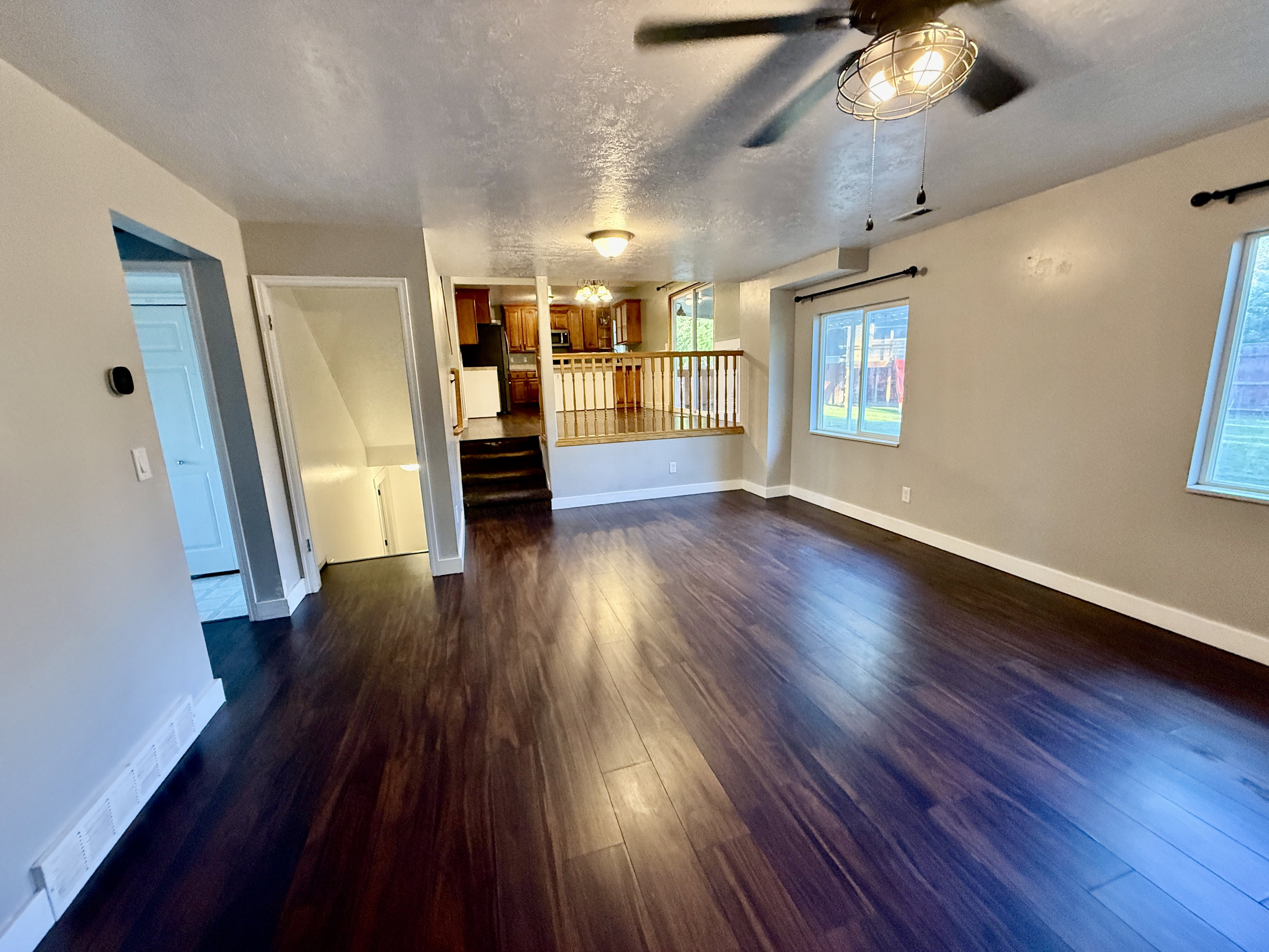 Spacious living area featuring dark wood-finish flooring, neutral wall tones, and a ceiling fan with industrial-style lighting