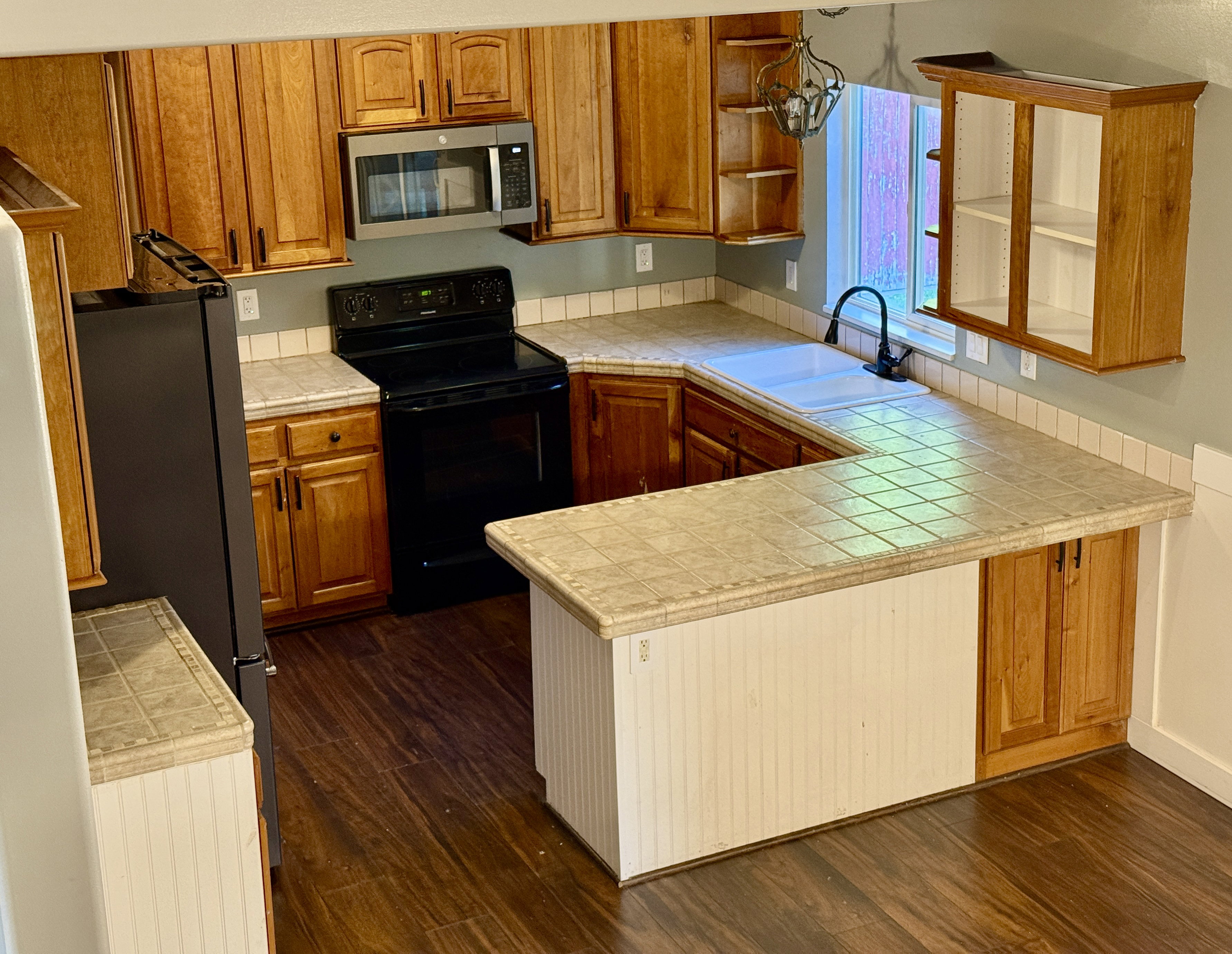 U-shaped kitchen featuring wood-finish cabinetry, tile countertops with a matching backsplash, and wood-finish flooring