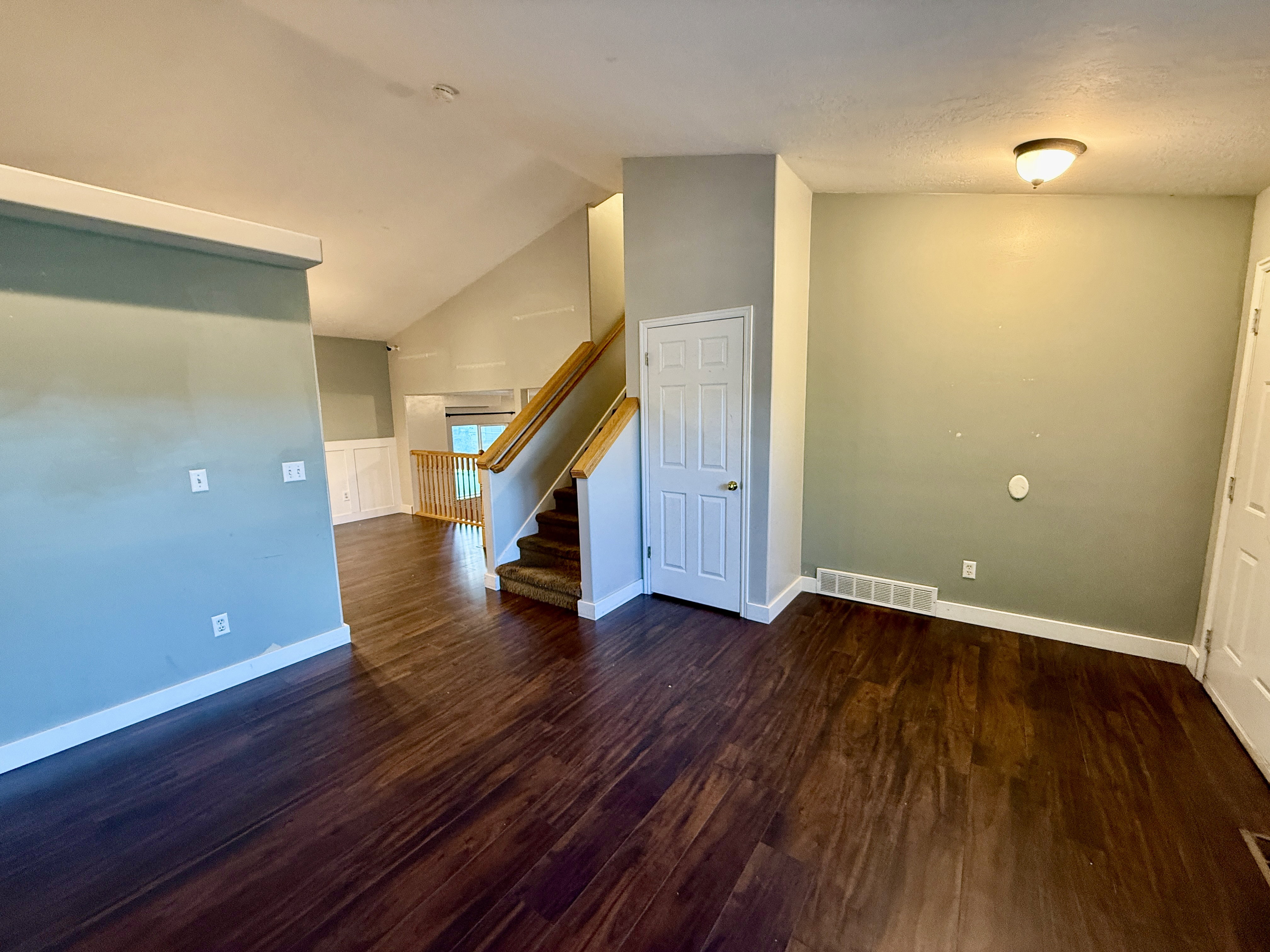 Interior space featuring dark wood-finish flooring, vaulted ceilings, and a carpeted staircase with wood handrails