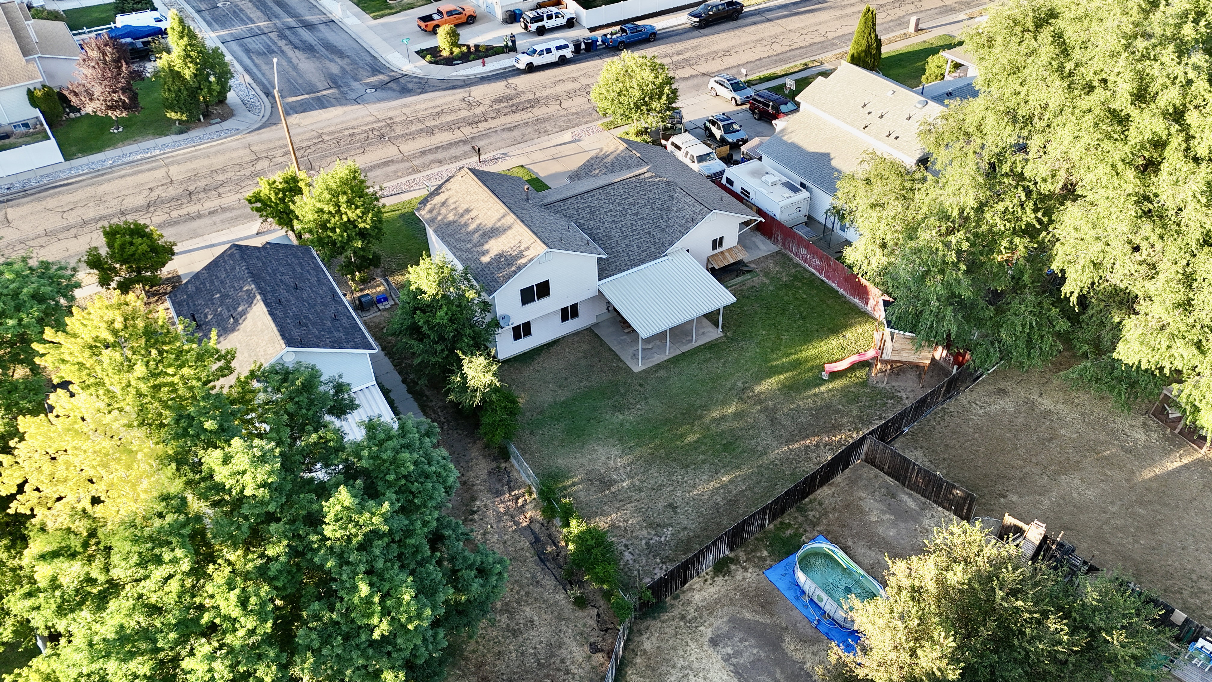 Expansive rear yard featuring a covered patio, mature trees, and a wooden privacy fence