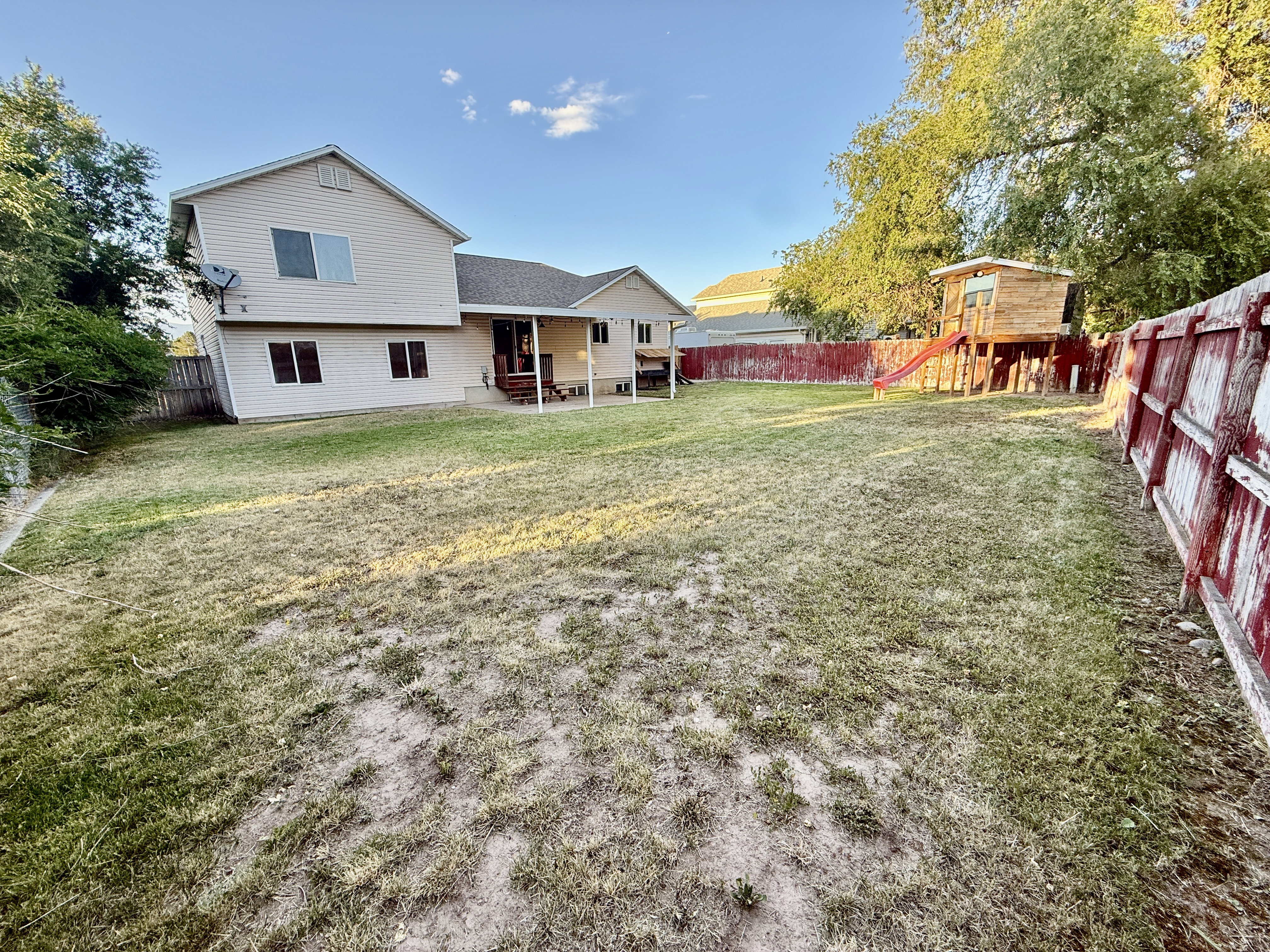 Spacious backyard featuring a large grass area, wood privacy fencing, and a covered patio directly accessing the rear of the home