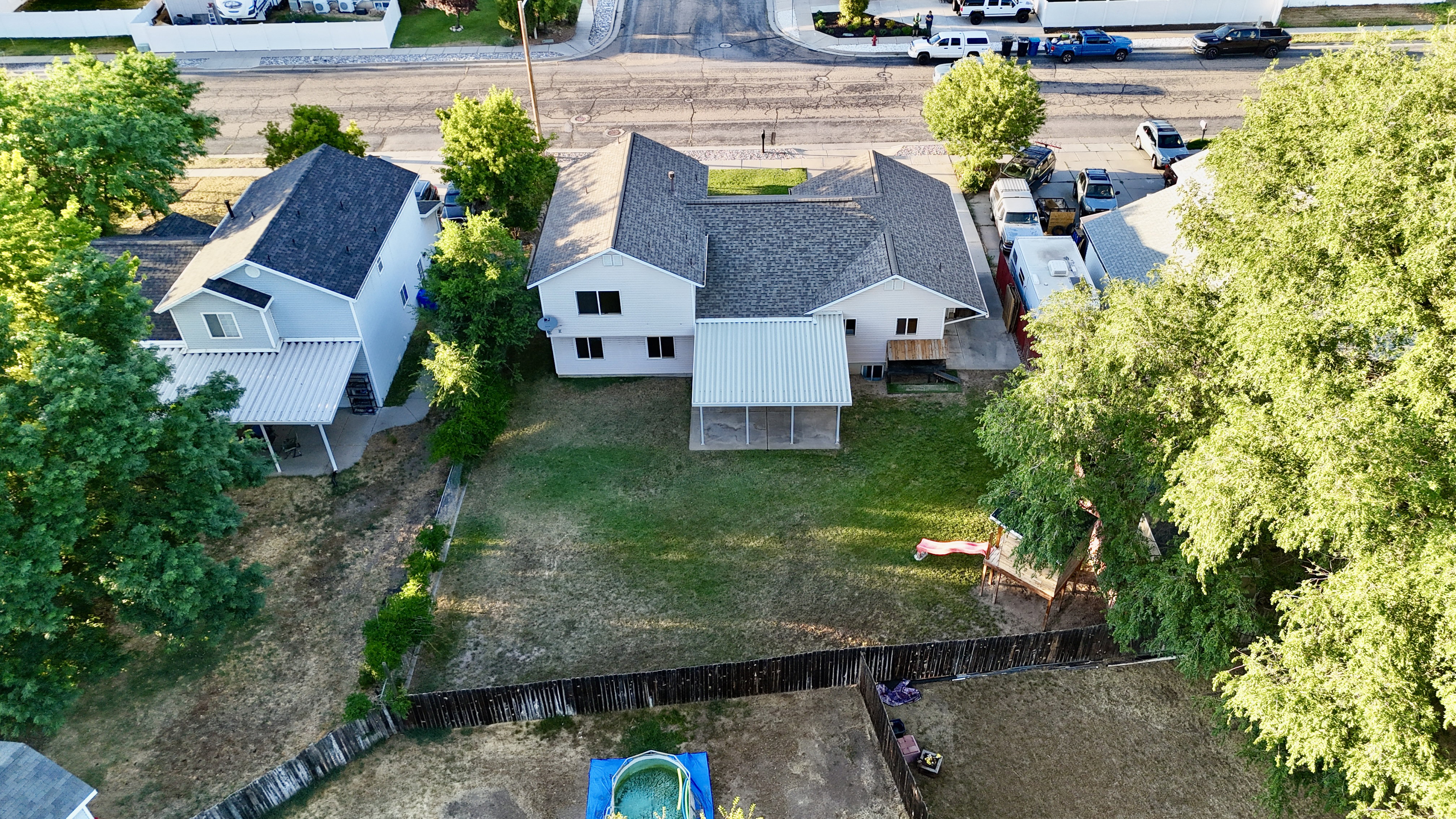Expansive backyard featuring a large green space, mature trees, and a wooden privacy fence