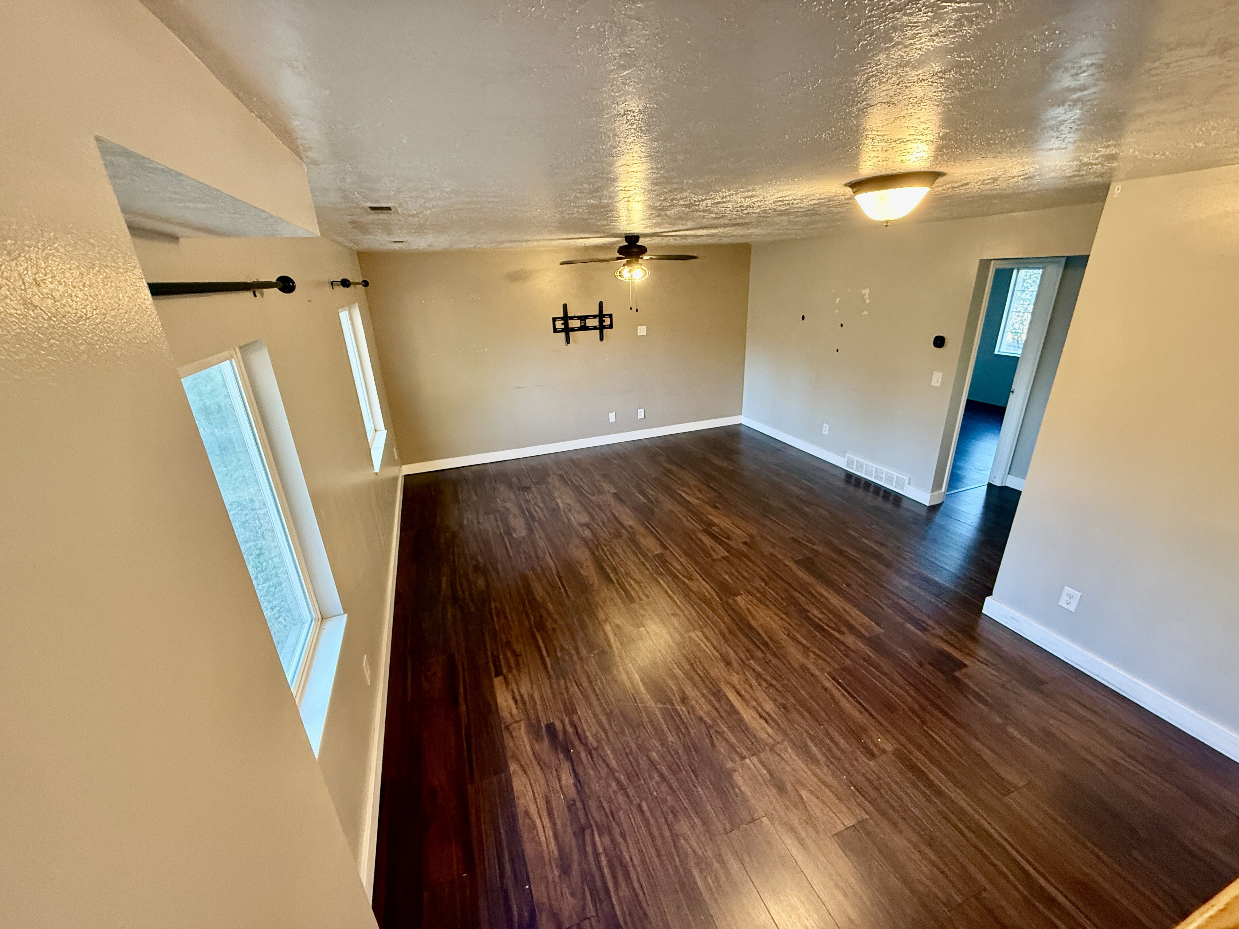 Spacious living area featuring rich wood-finish flooring, a ceiling fan, and multiple windows providing natural light