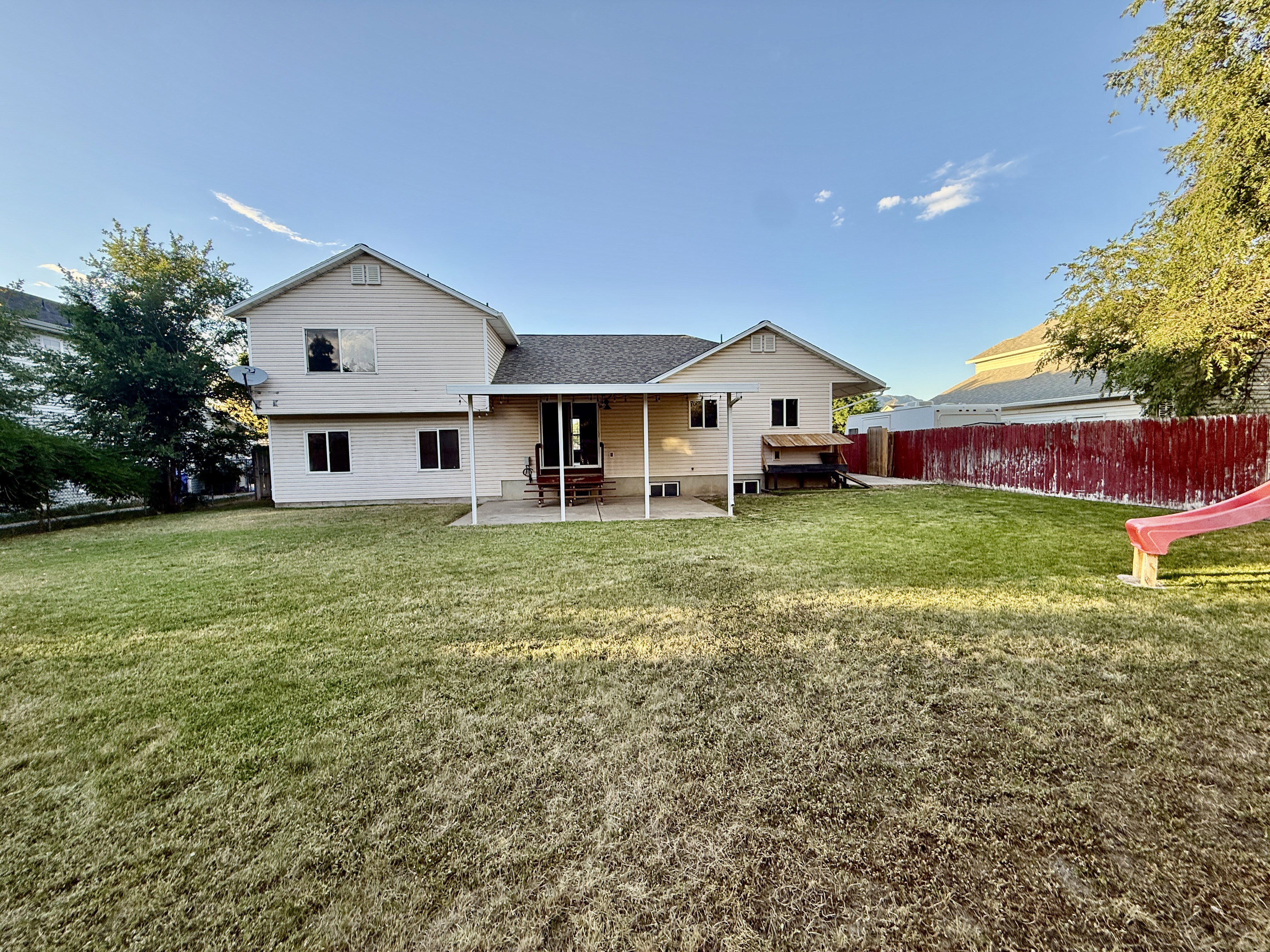 Expansive backyard featuring a manicured lawn, a covered patio, and mature trees