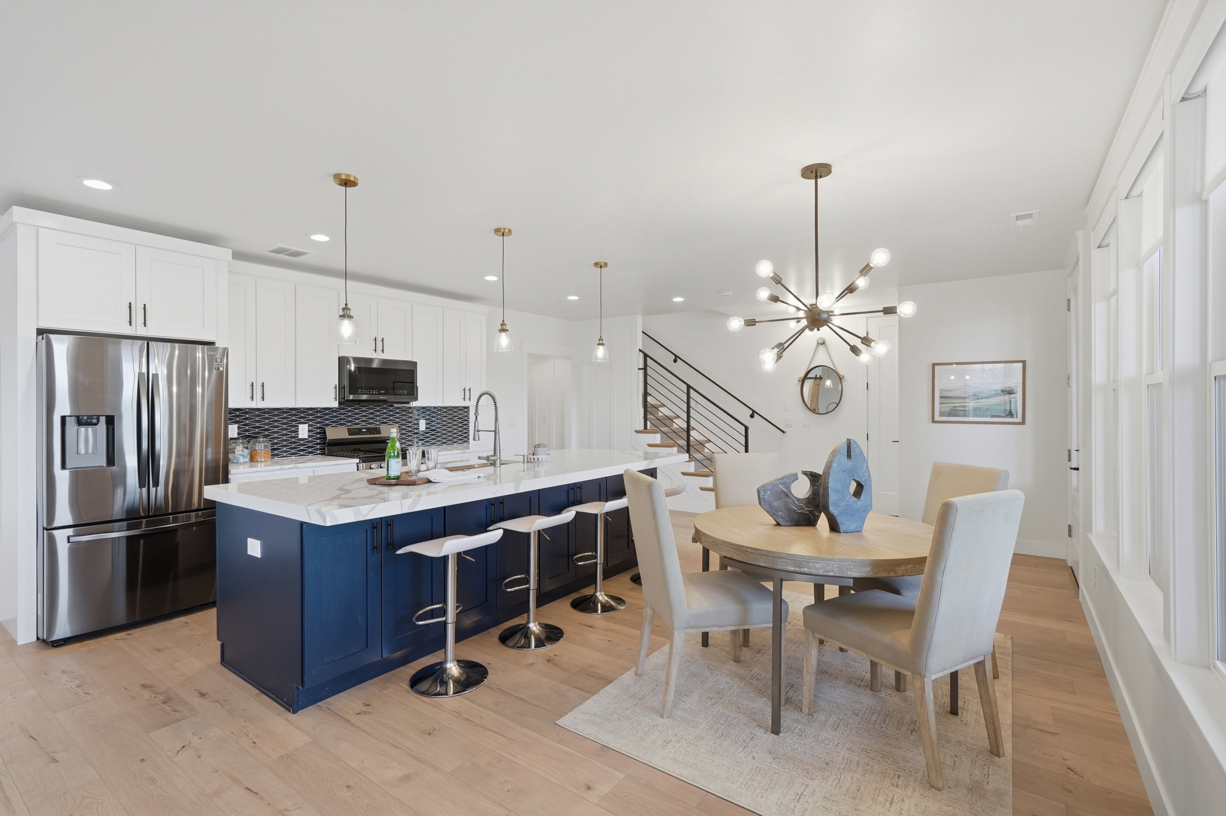 Open-concept kitchen and dining area featuring a spacious island with seating, stainless steel appliances, a tile backsplash, and light wood-finish flooring