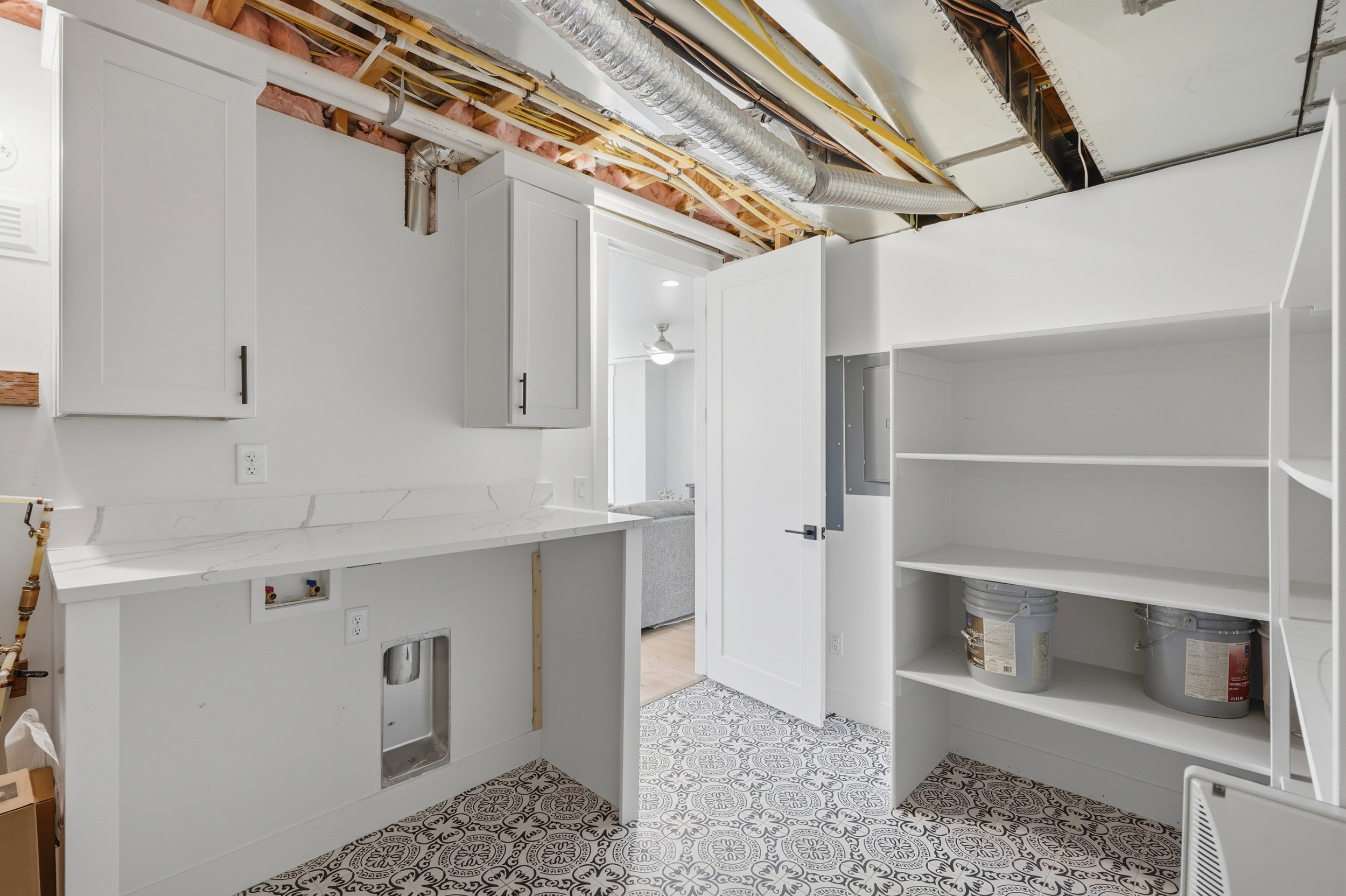 Laundry area with patterned floor tiles, white cabinetry, a countertop, and open shelving