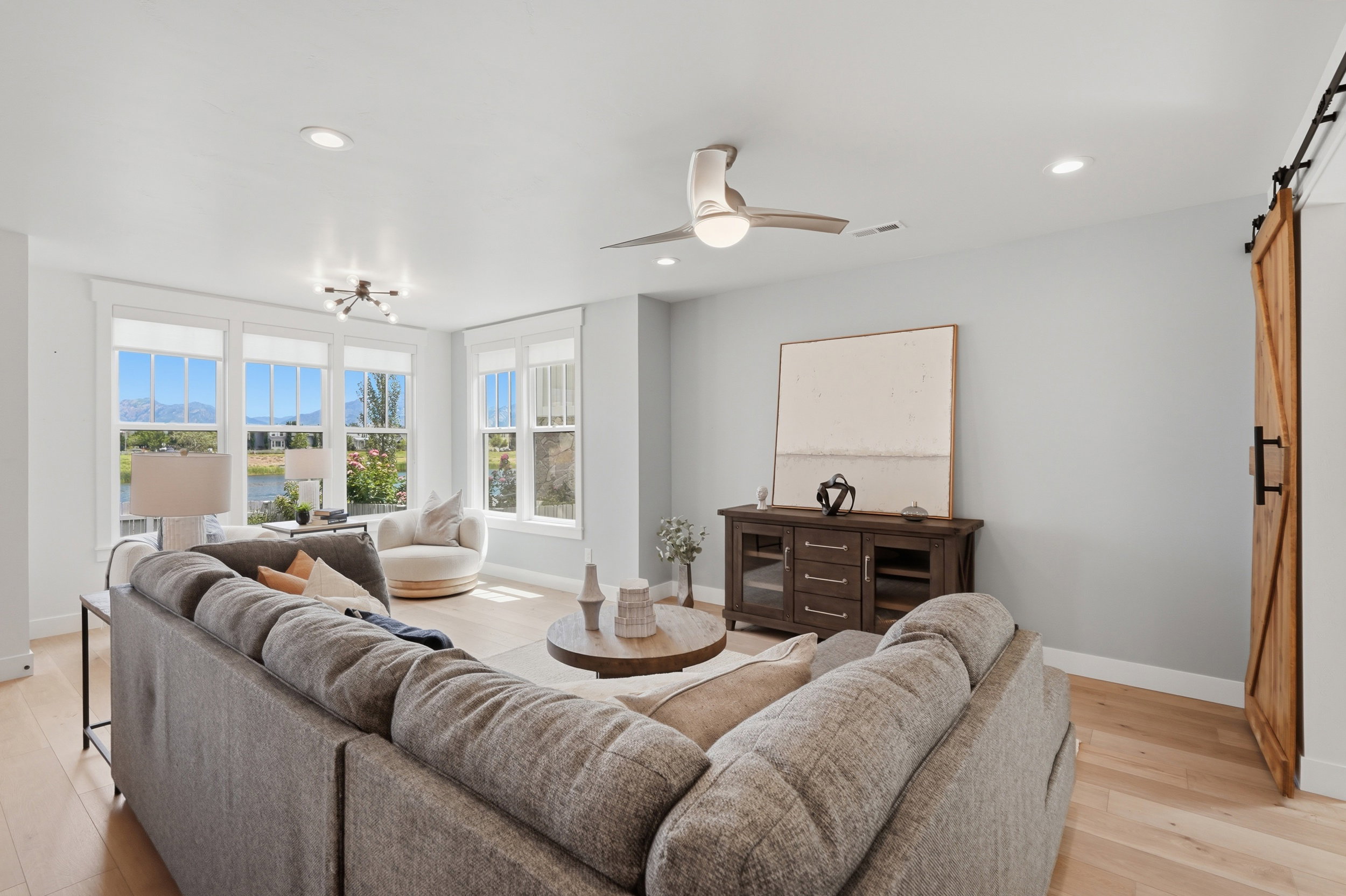 Spacious living area featuring light wood-finish flooring and ample natural light from multiple large windows