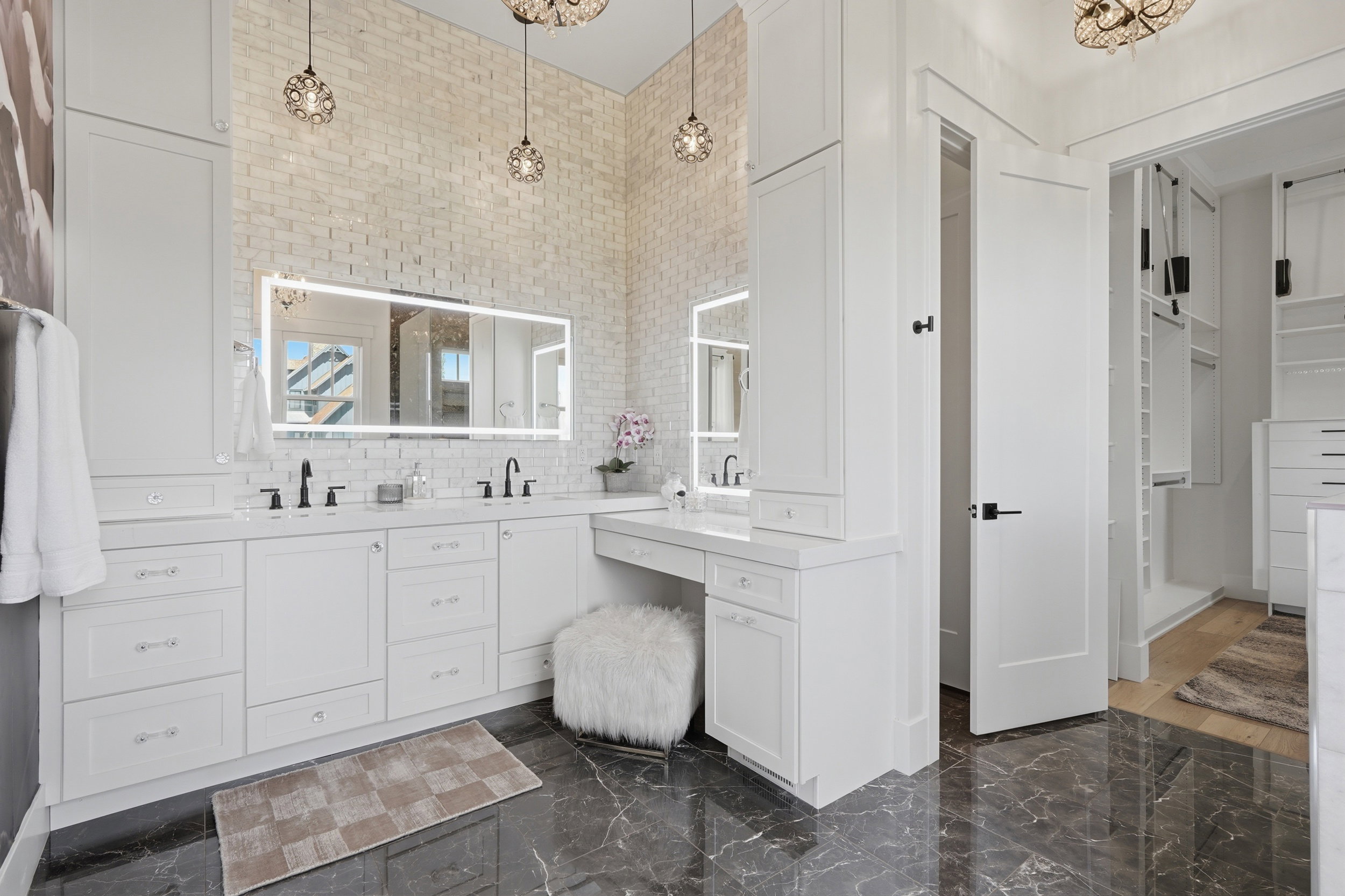 White brick accent wall with a large backlit mirror over a double vanity, featuring matte black fixtures and ample cabinetry