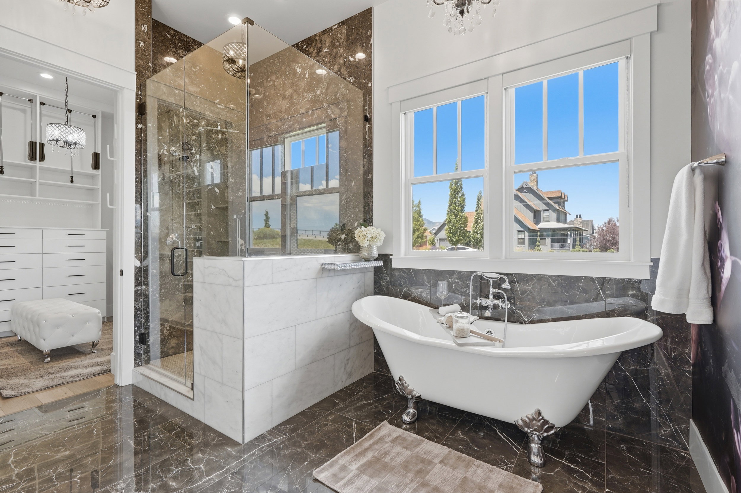 Freestanding clawfoot tub with a chrome faucet set, glass-enclosed shower, and dark marble-finish flooring