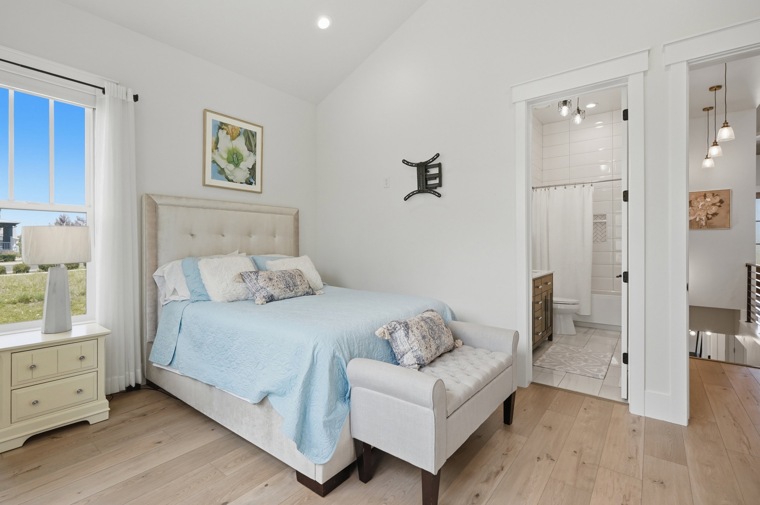 Vaulted ceiling bedroom featuring wood-finish flooring and a large window