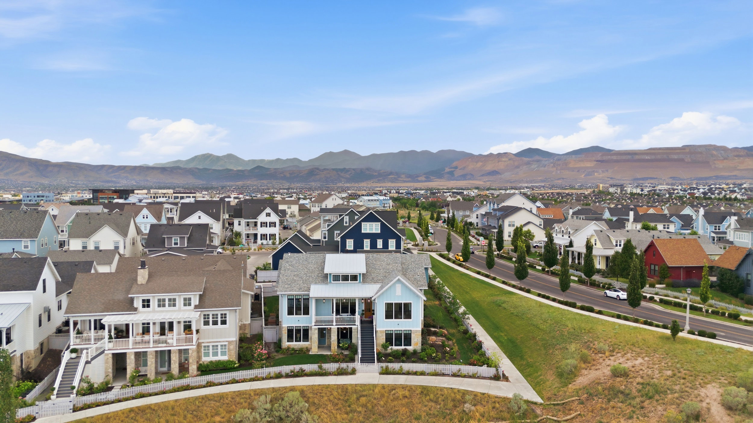 Contemporary residential community featuring diverse architectural styles, tree-lined streets, and mountain terrain in the background