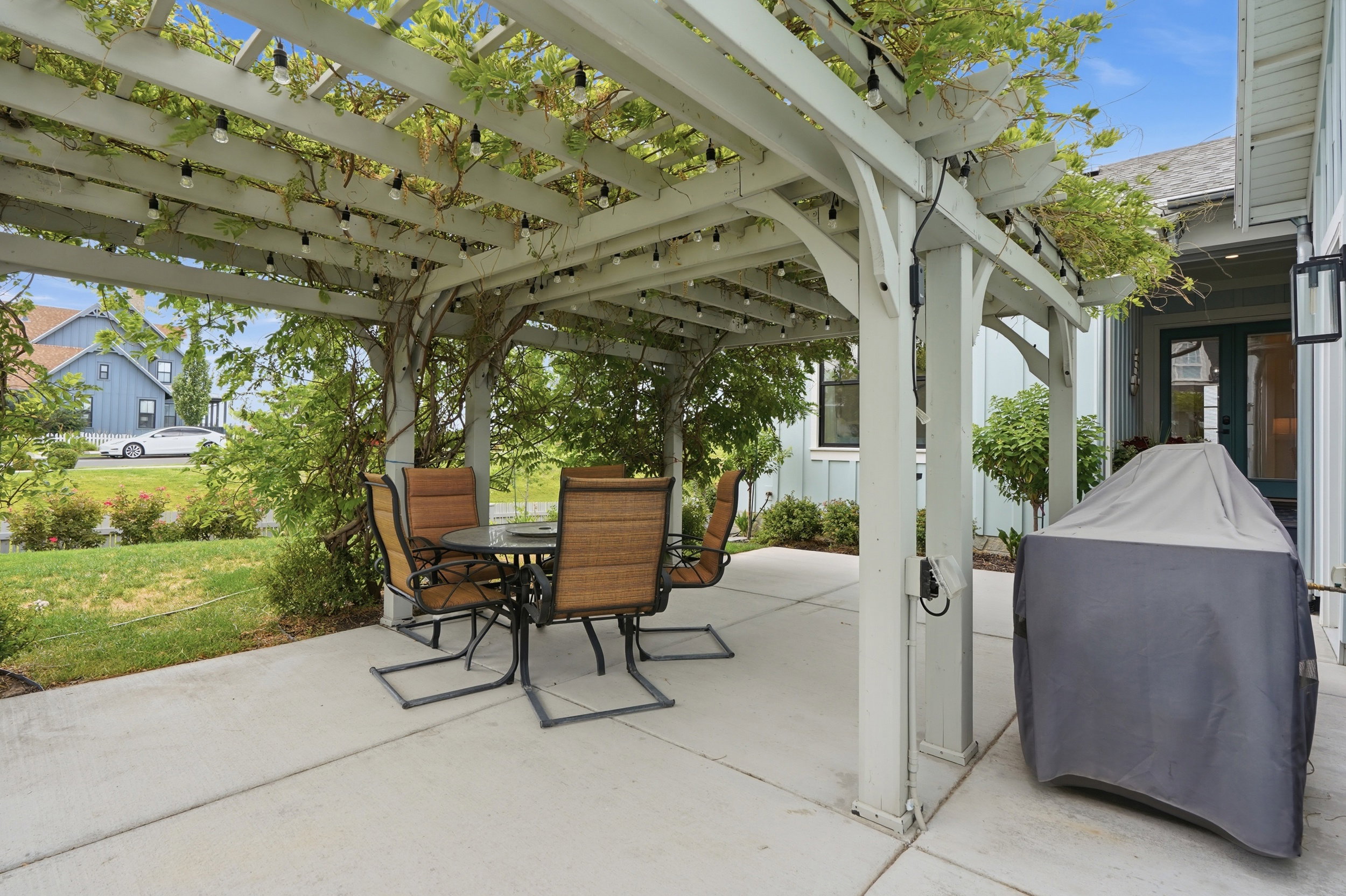 Outdoor concrete patio featuring a white pergola with string lights and established climbing foliage