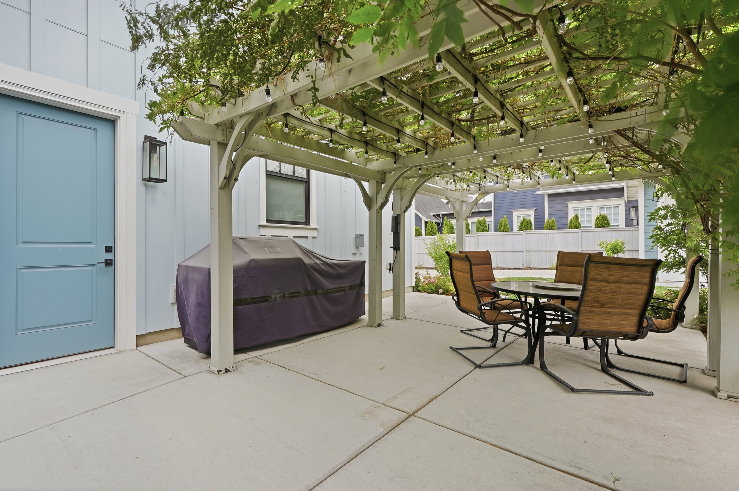 Spacious concrete patio featuring a white pergola with overhead string lighting and lush vine coverage