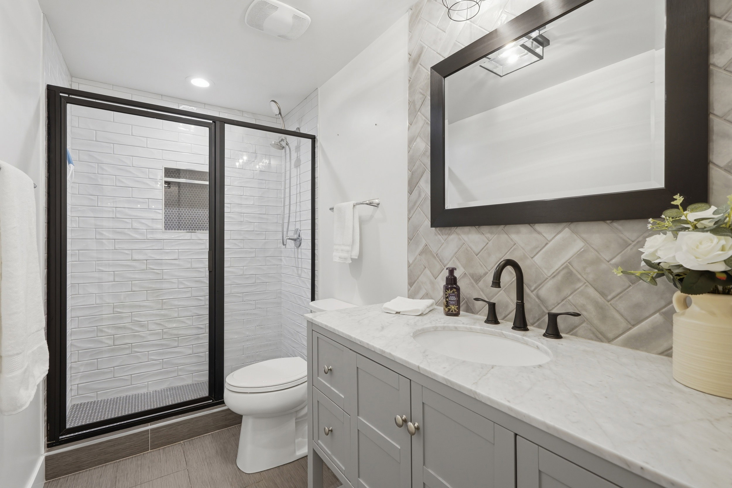 Modern bathroom featuring a single vanity with a marble-finish countertop, undermount sink, and dark bronze-finish fixtures