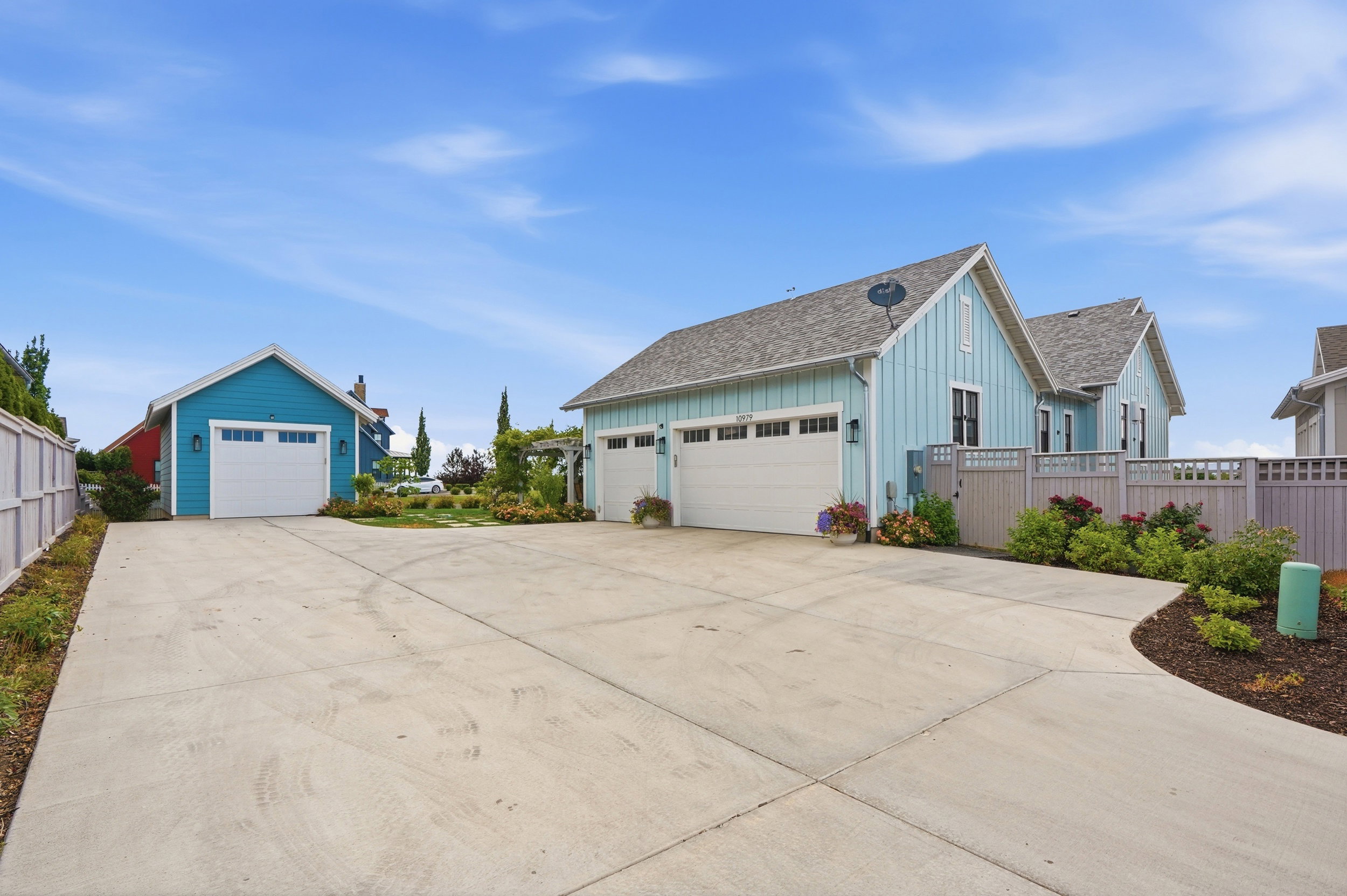 Expansive concrete driveway with two detached structures featuring horizontal siding and white garage doors