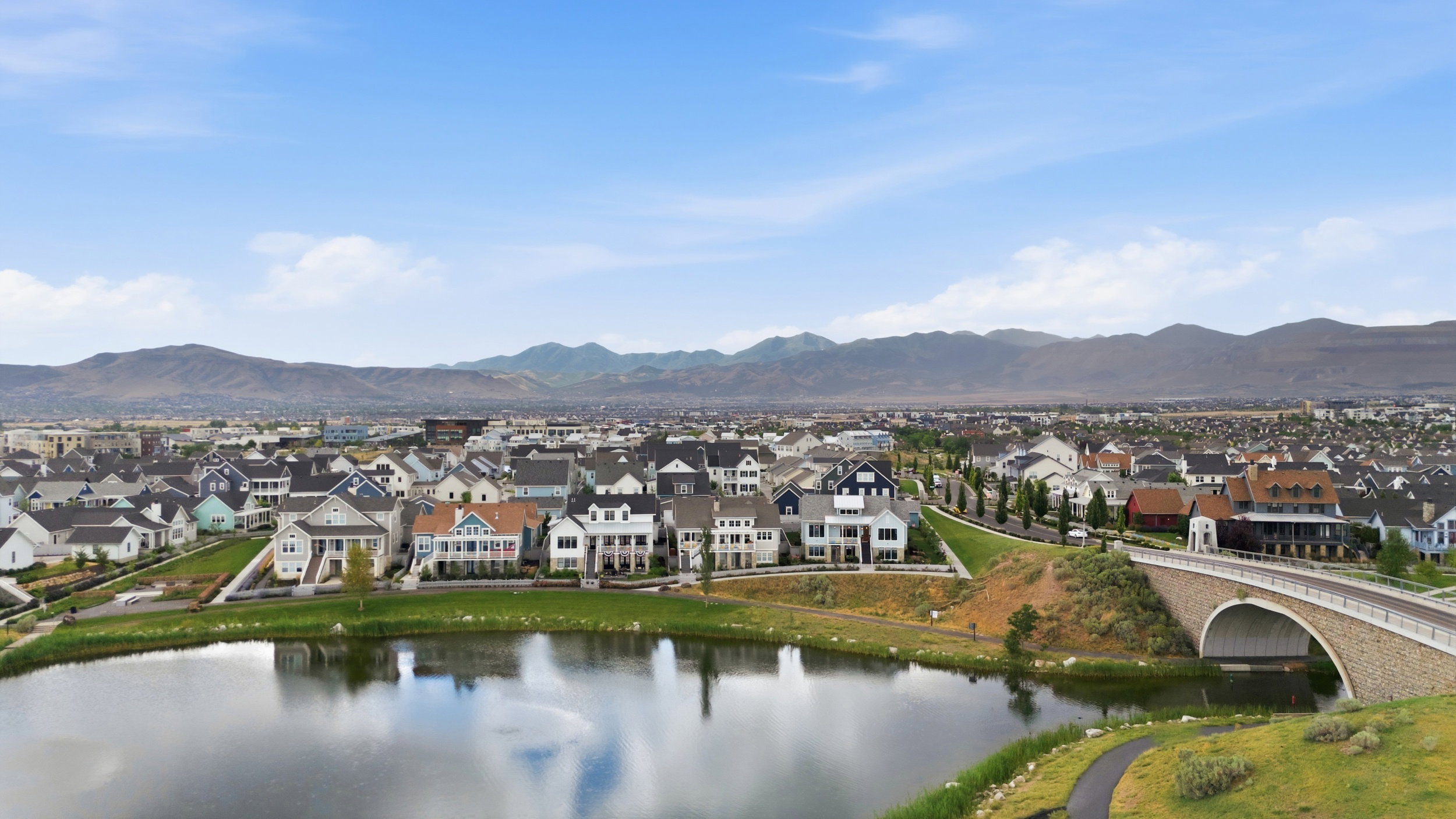 Expansive community featuring diverse architectural styles, a large reflective pond, and a stone arch bridge