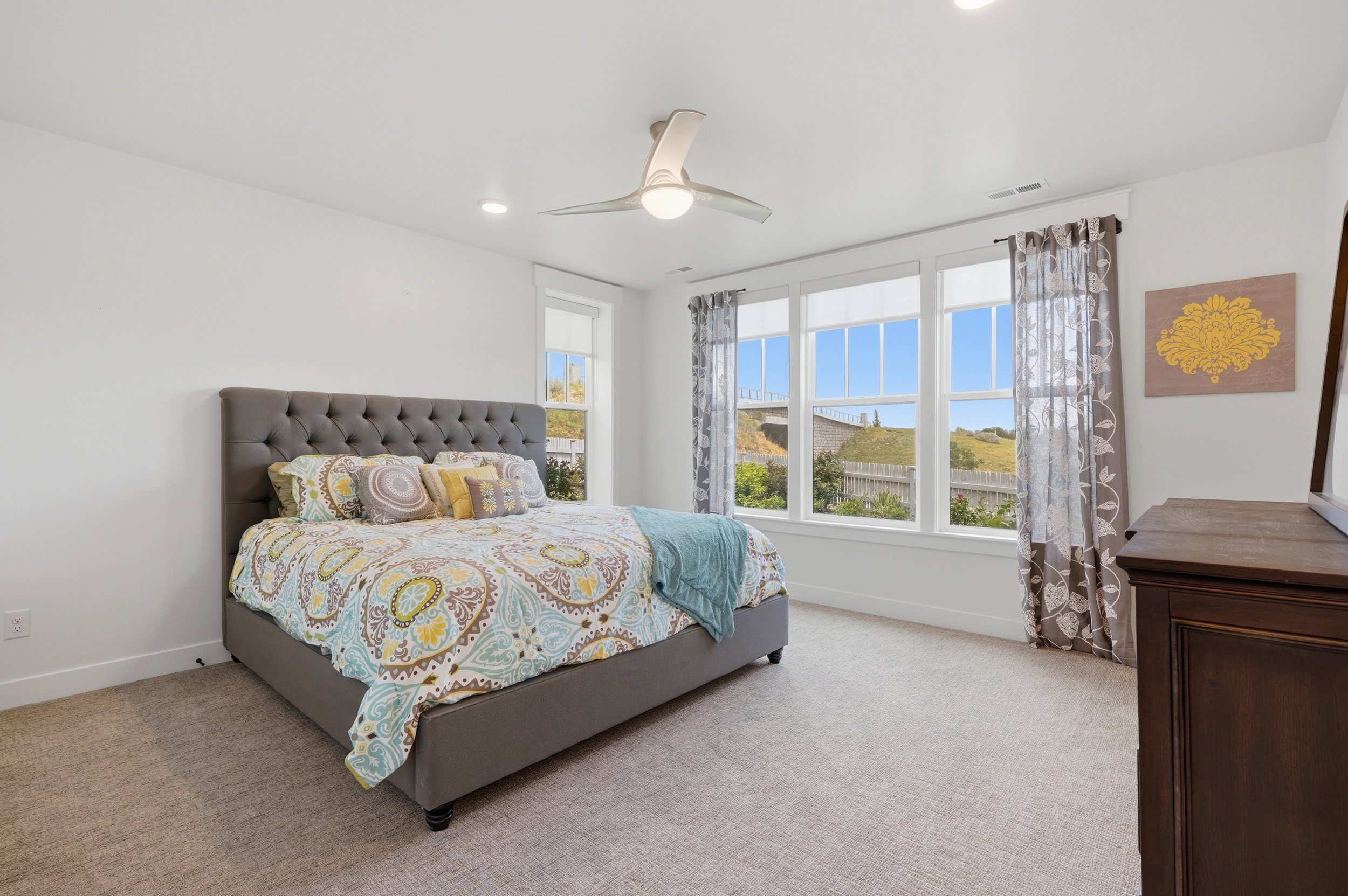 Carpeted bedroom featuring white walls, a multi-pane window configuration, and a ceiling fan with integrated lighting