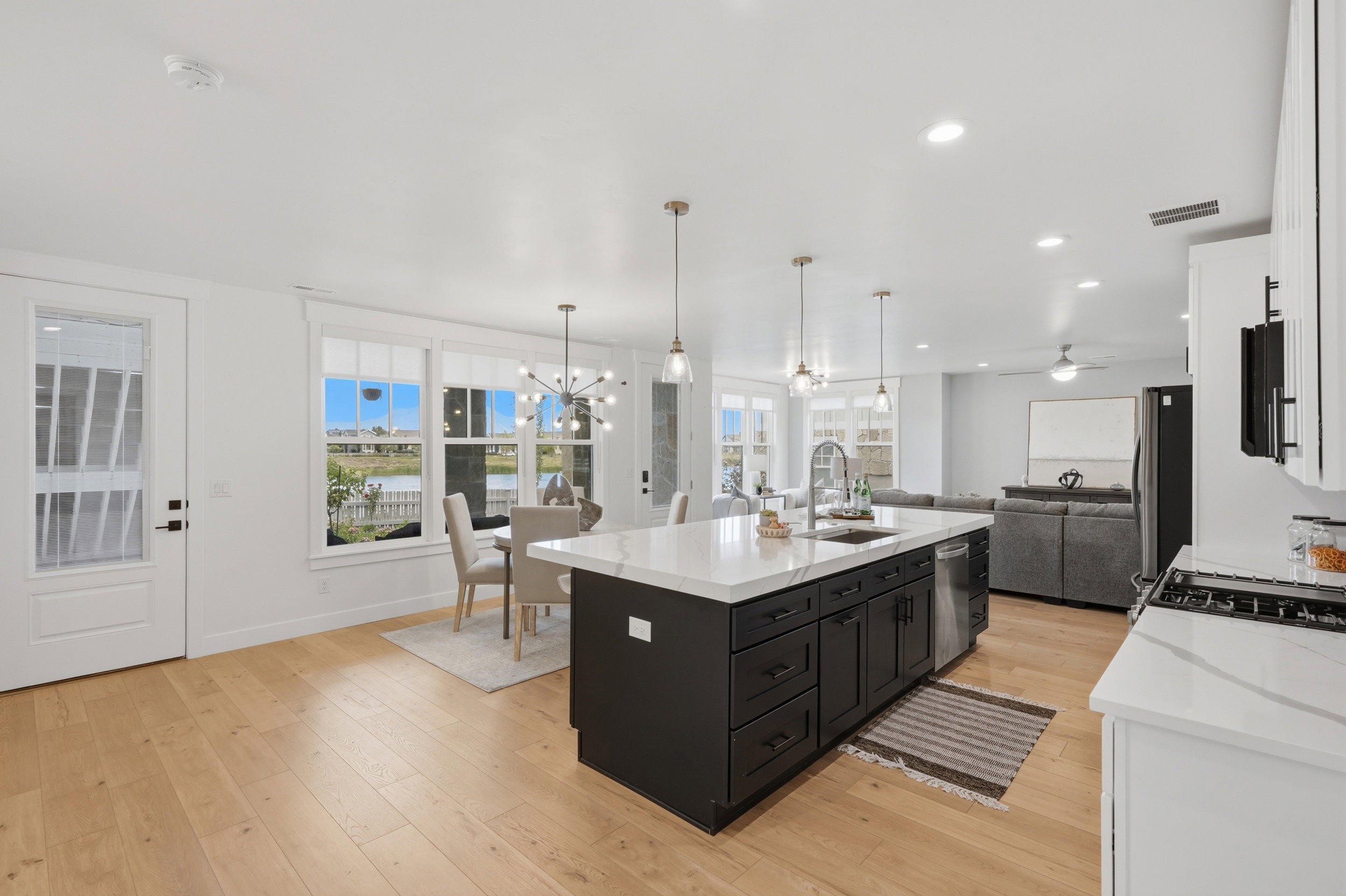 Open-concept living space featuring wood-finish flooring, a kitchen island with stone countertop, recessed lighting, and a dining area with a contemporary chandelier