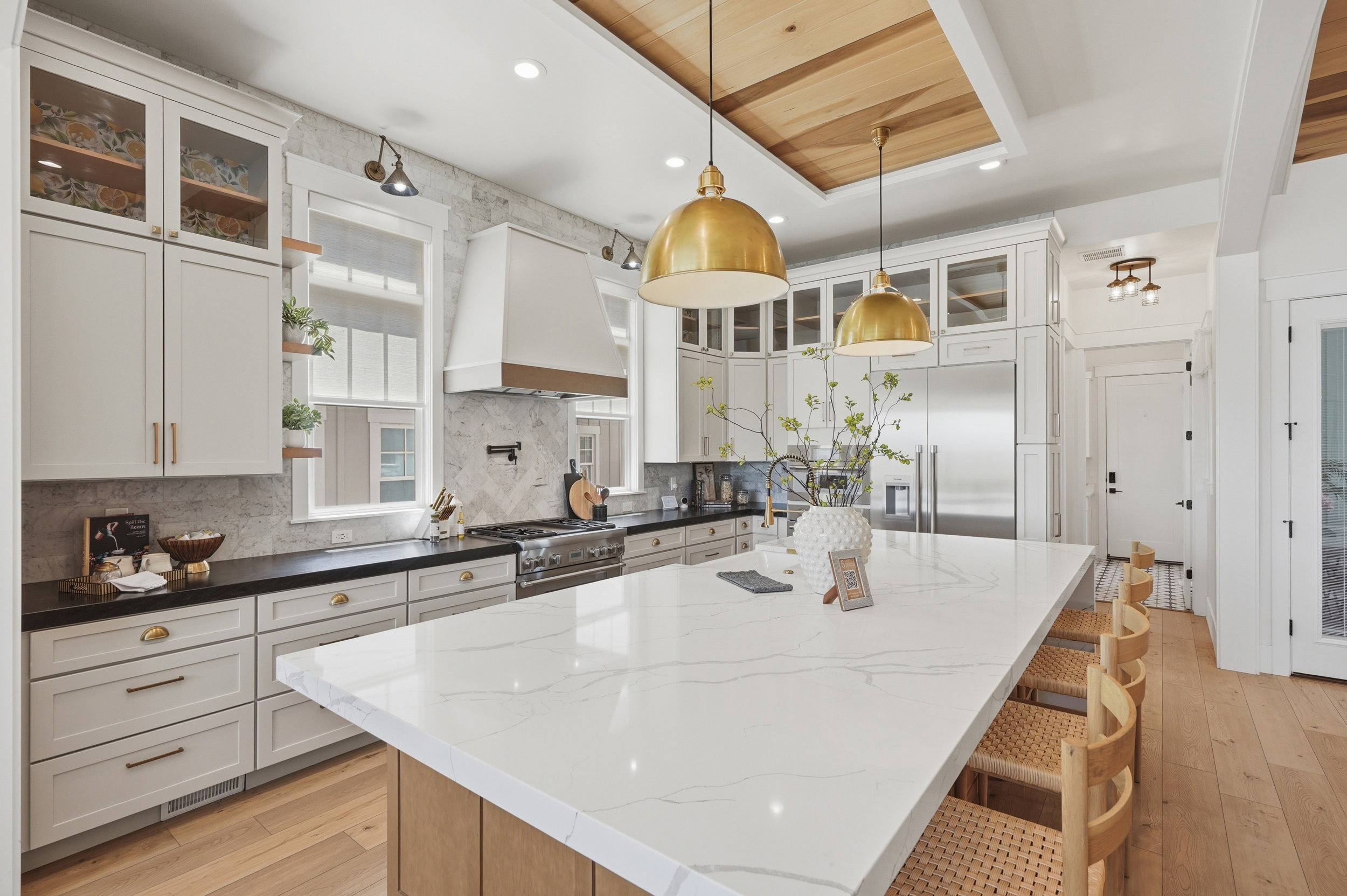 Gourmet kitchen featuring a substantial center island with seating, stainless steel appliances, custom cabinetry, a stylish range hood, and wood-finish flooring