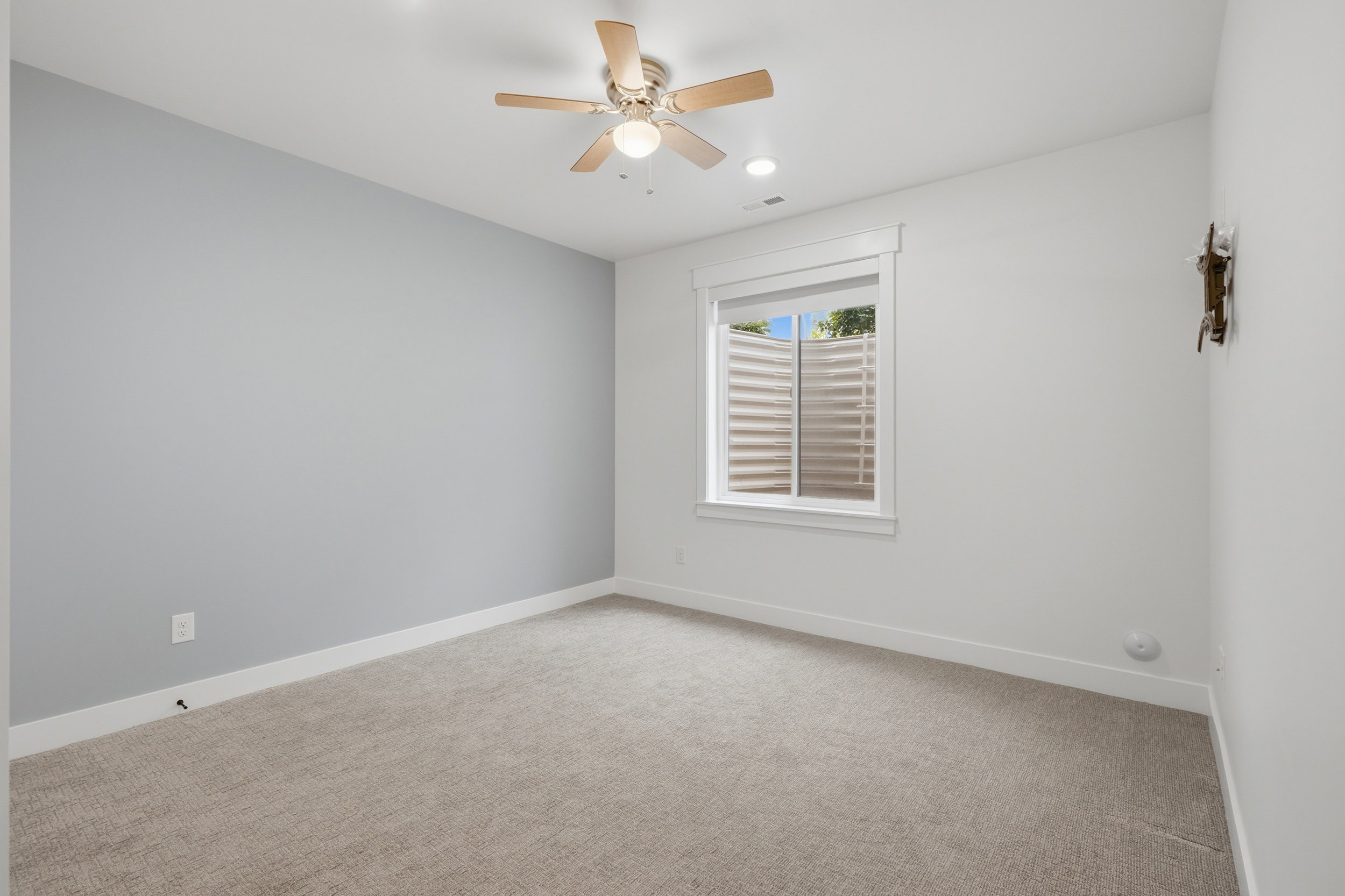Carpeted room featuring a light gray accent wall, white baseboards, and a window with horizontal blinds