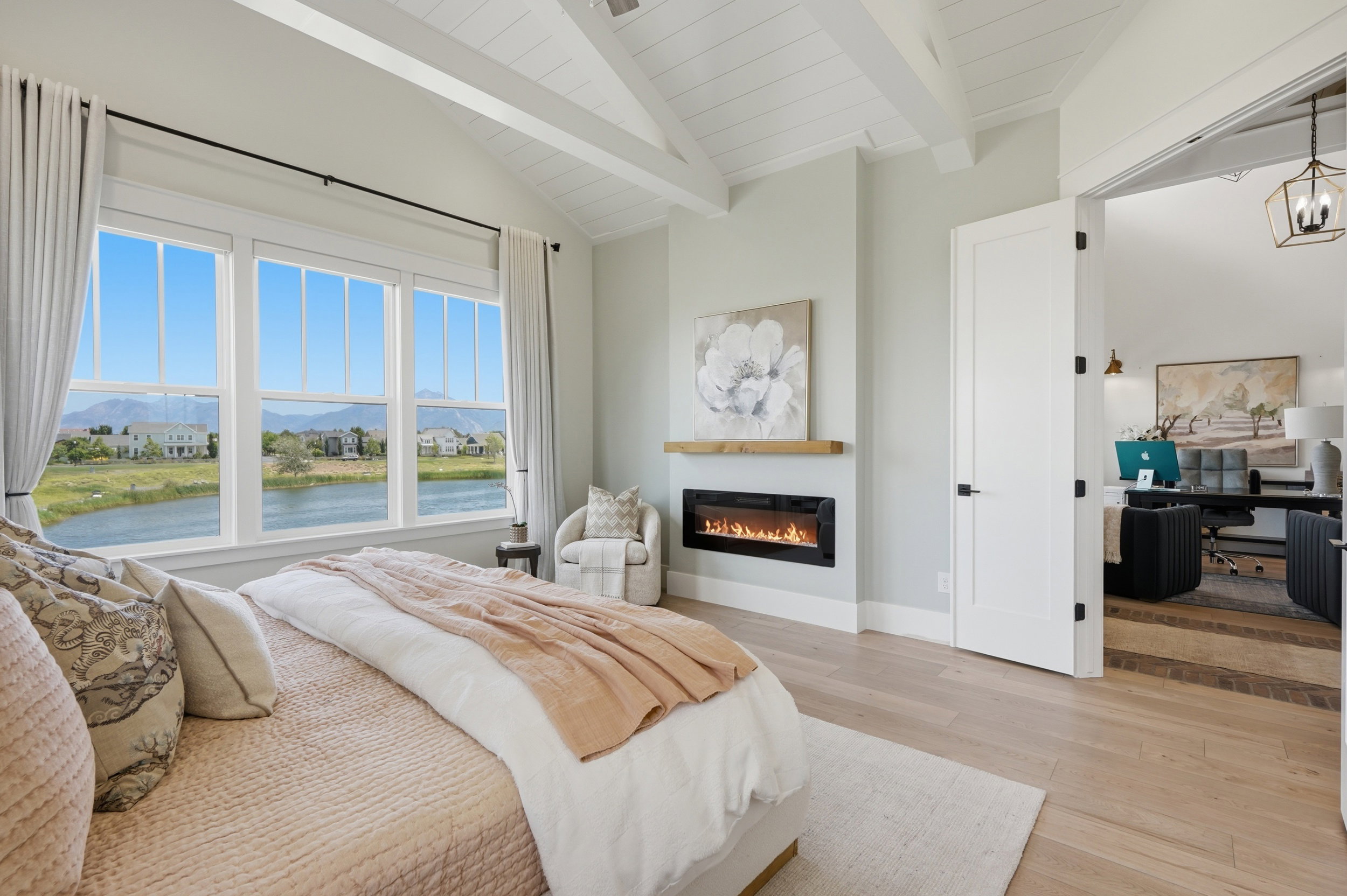Vaulted ceiling with exposed beams, wood-finish flooring, and expansive windows offering water frontage